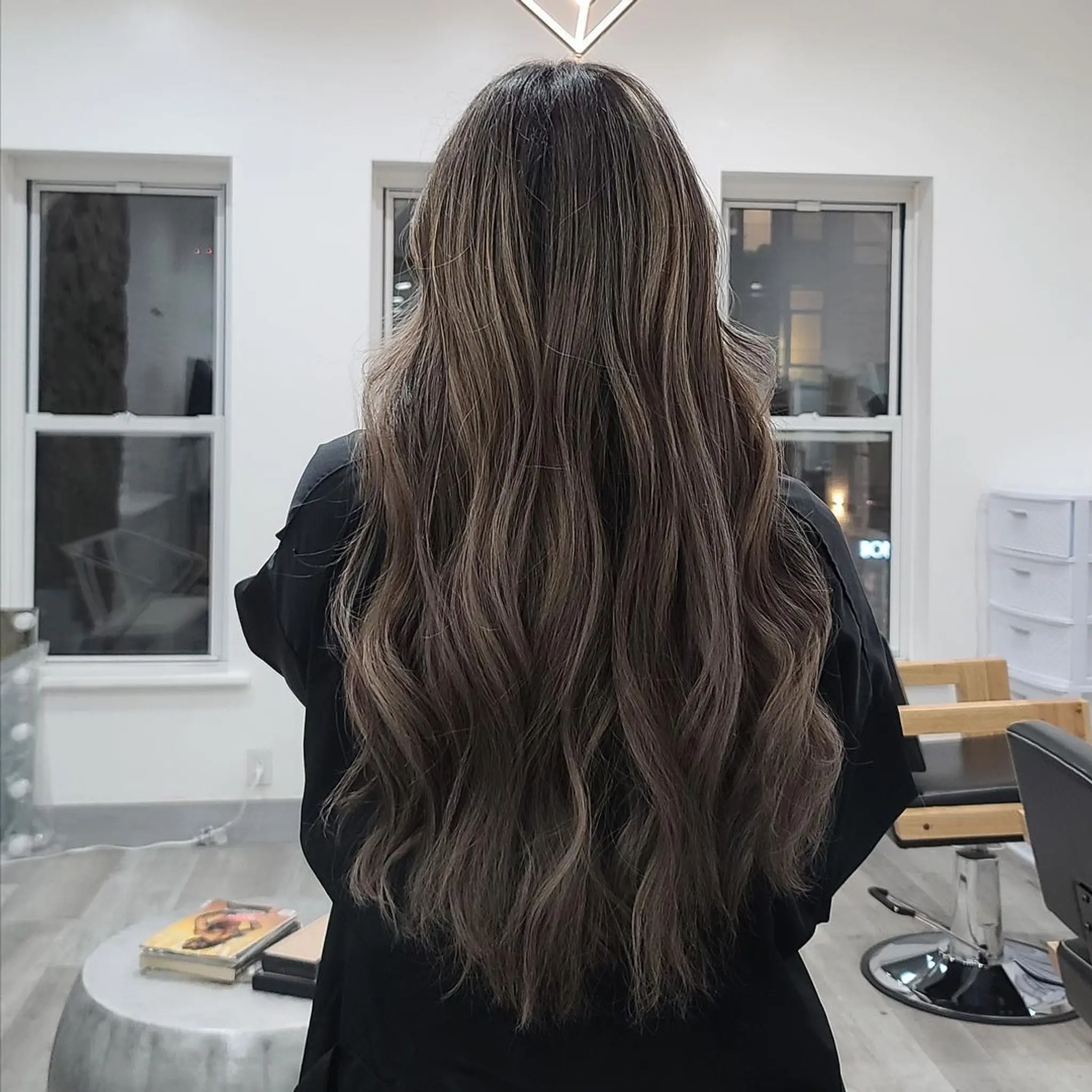 Very long, wavy ash brown hair with honey highlights and soft layers, enhanced by a balayage technique for added depth and volume.