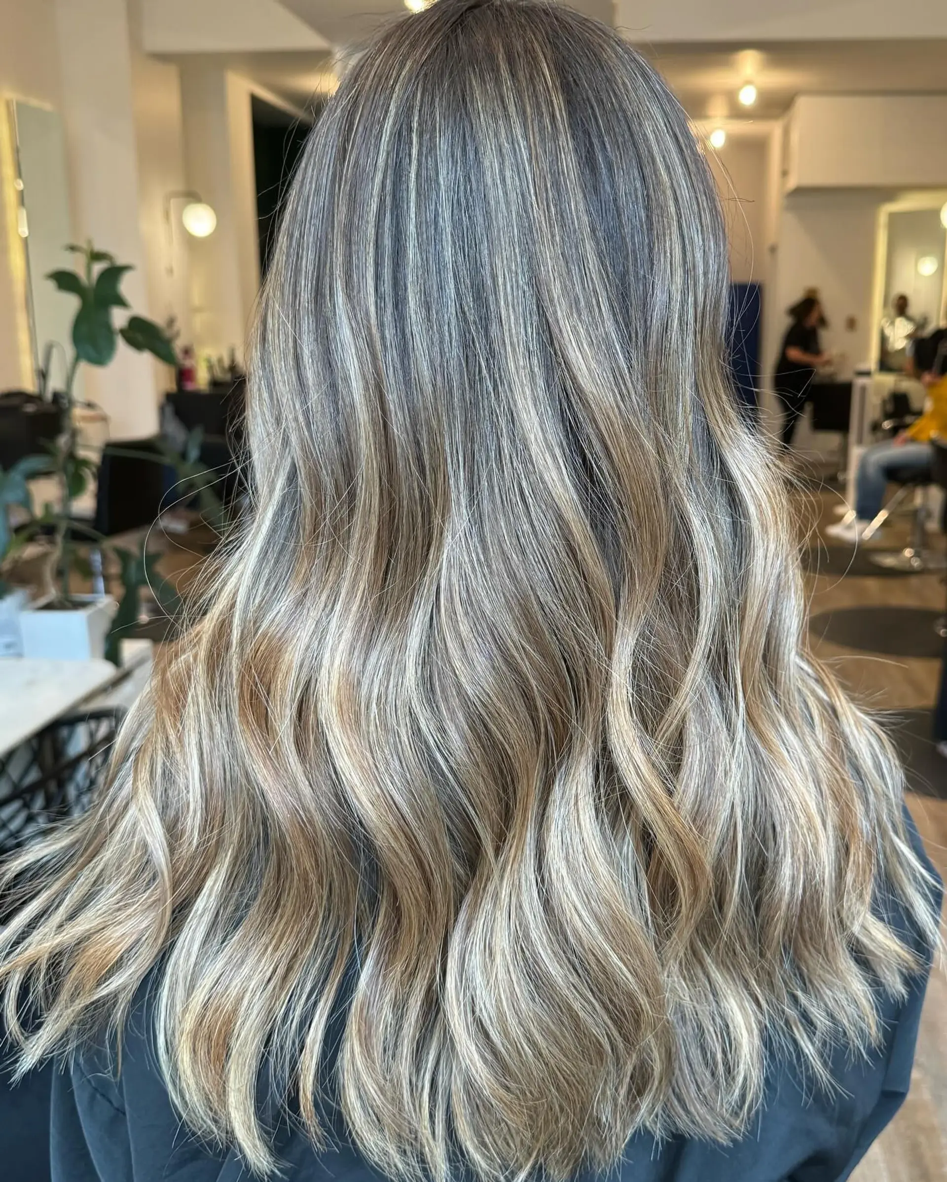 Long flowing hair styled in soft waves with dimensional cool ash blonde highlights blended throughout a light brown base. 1