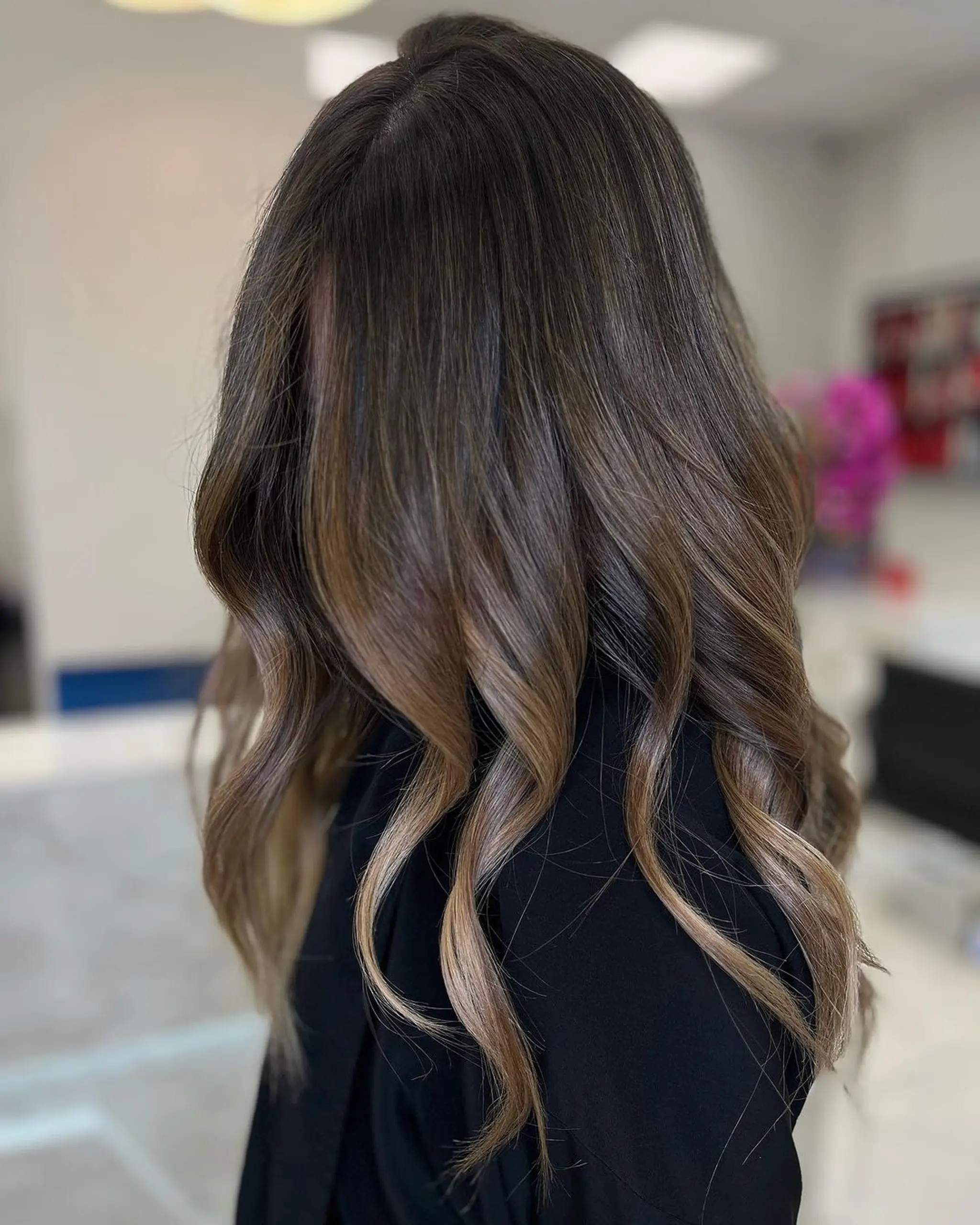 Long, wavy hair with a rich brown base and blonde balayage highlights, featuring loose, natural waves and layered for movement and volume.