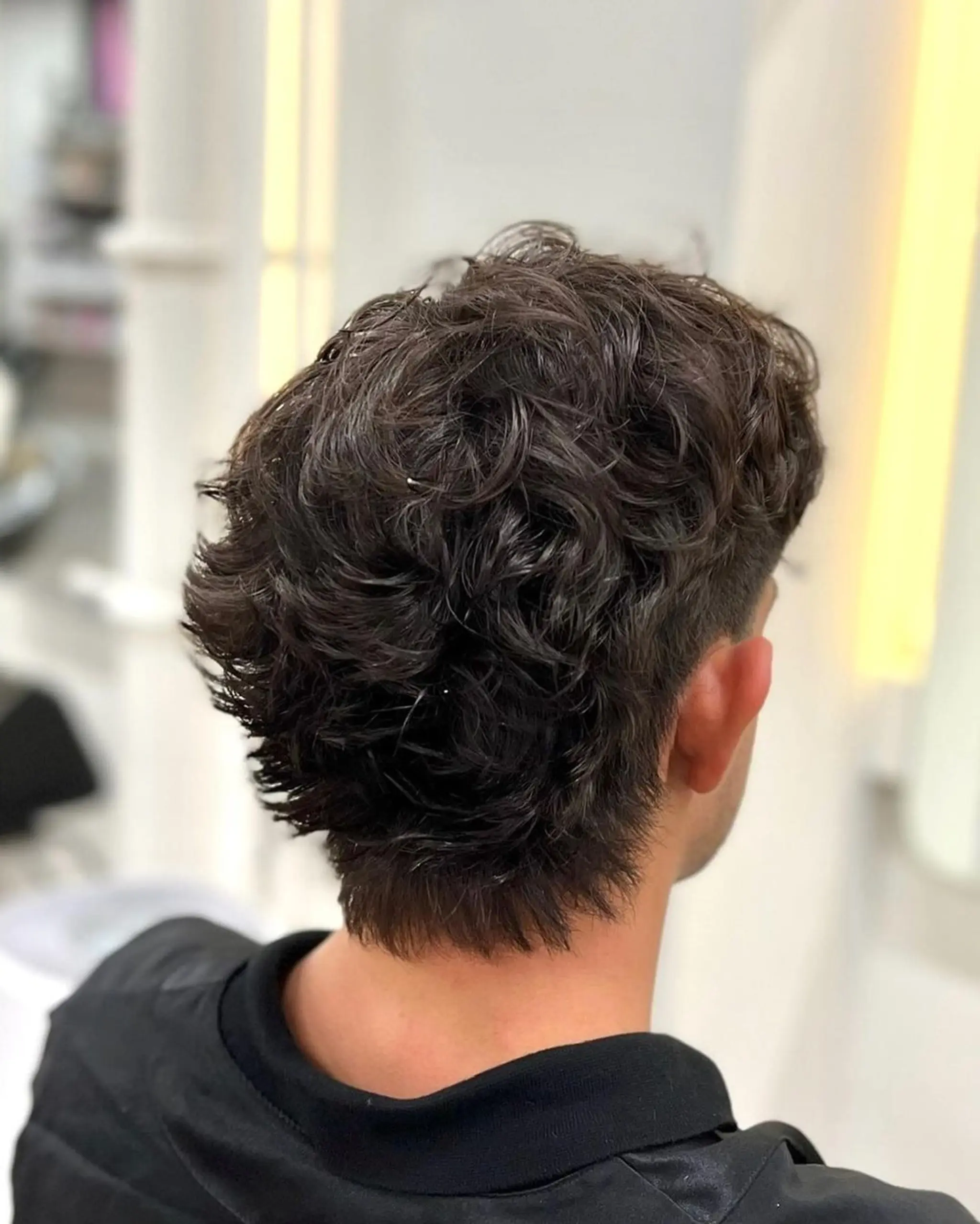 Medium-length dark brown hair with natural waves, layered and textured, with fuller sections at the crown and tapered sides.