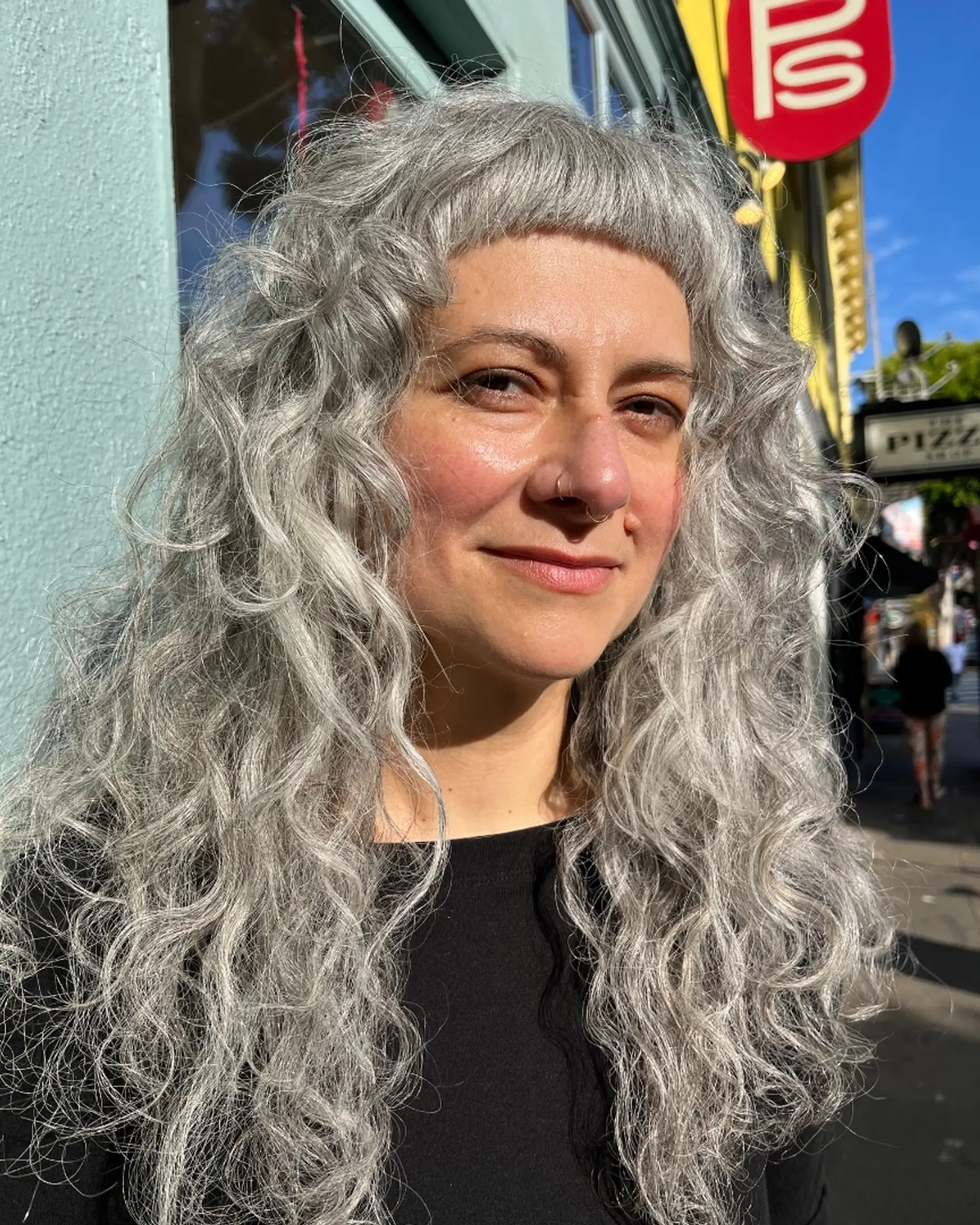 Long silver curly hair styled with short straight-cut micro bangs. 1