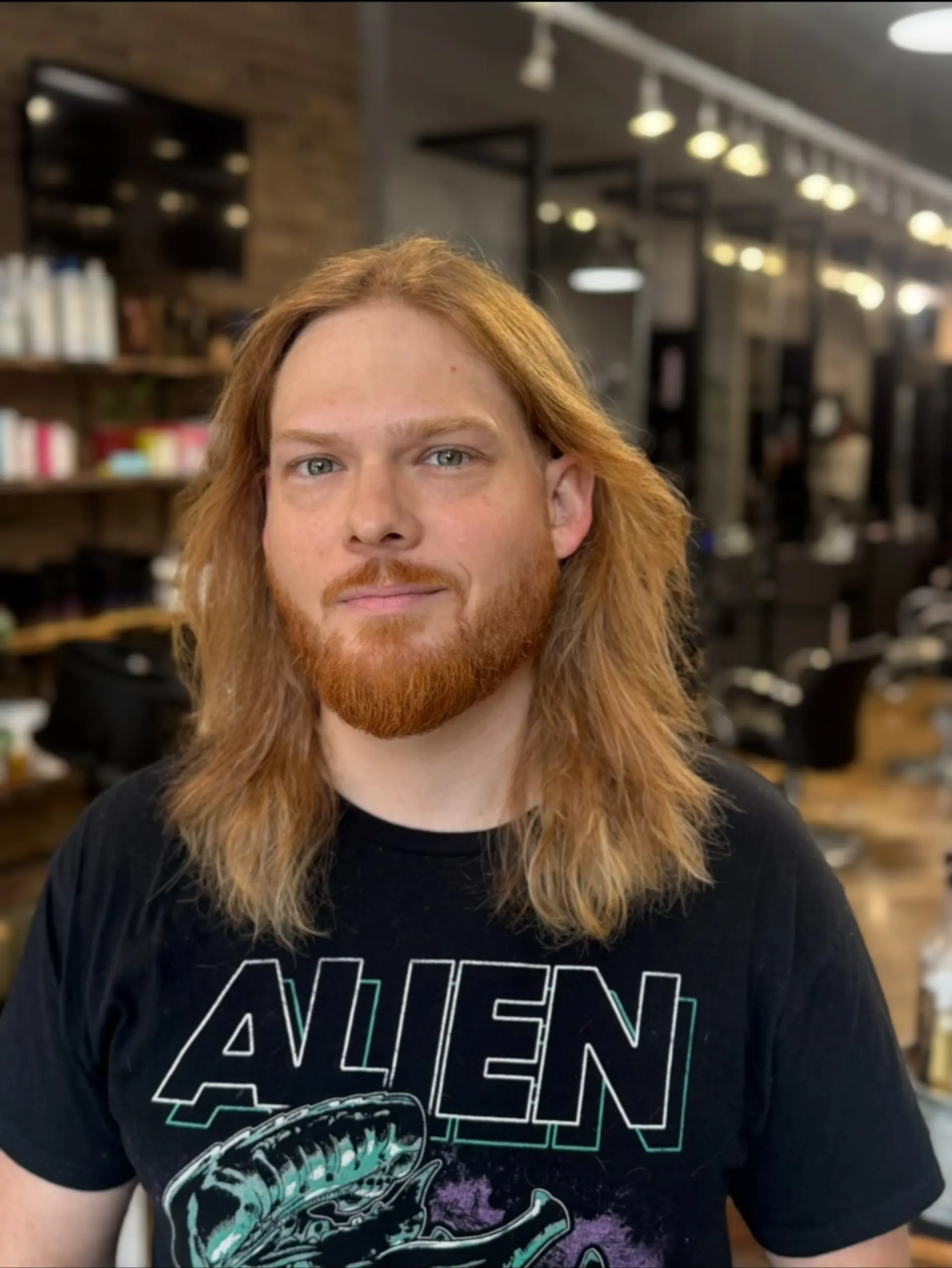 Shoulder-skimming layered strawberry blonde hair parted down the middle, styled naturally with soft movement and paired with a full groomed beard. 1
