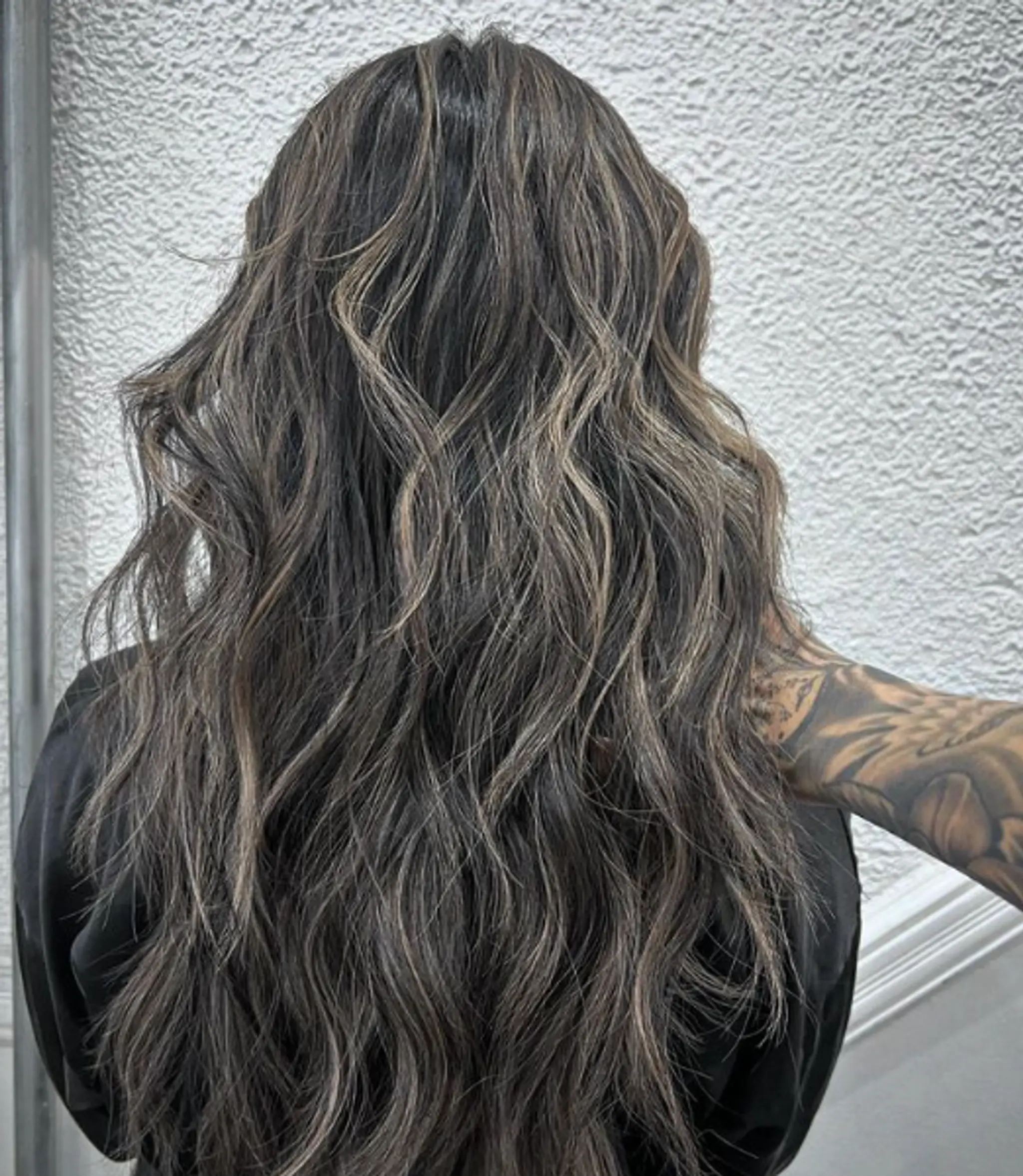 A very long, wavy hairstyle with a rich dark brown base and ash blonde highlights. The hair cascades in natural waves beyond the back, with layered cuts adding depth and movement.