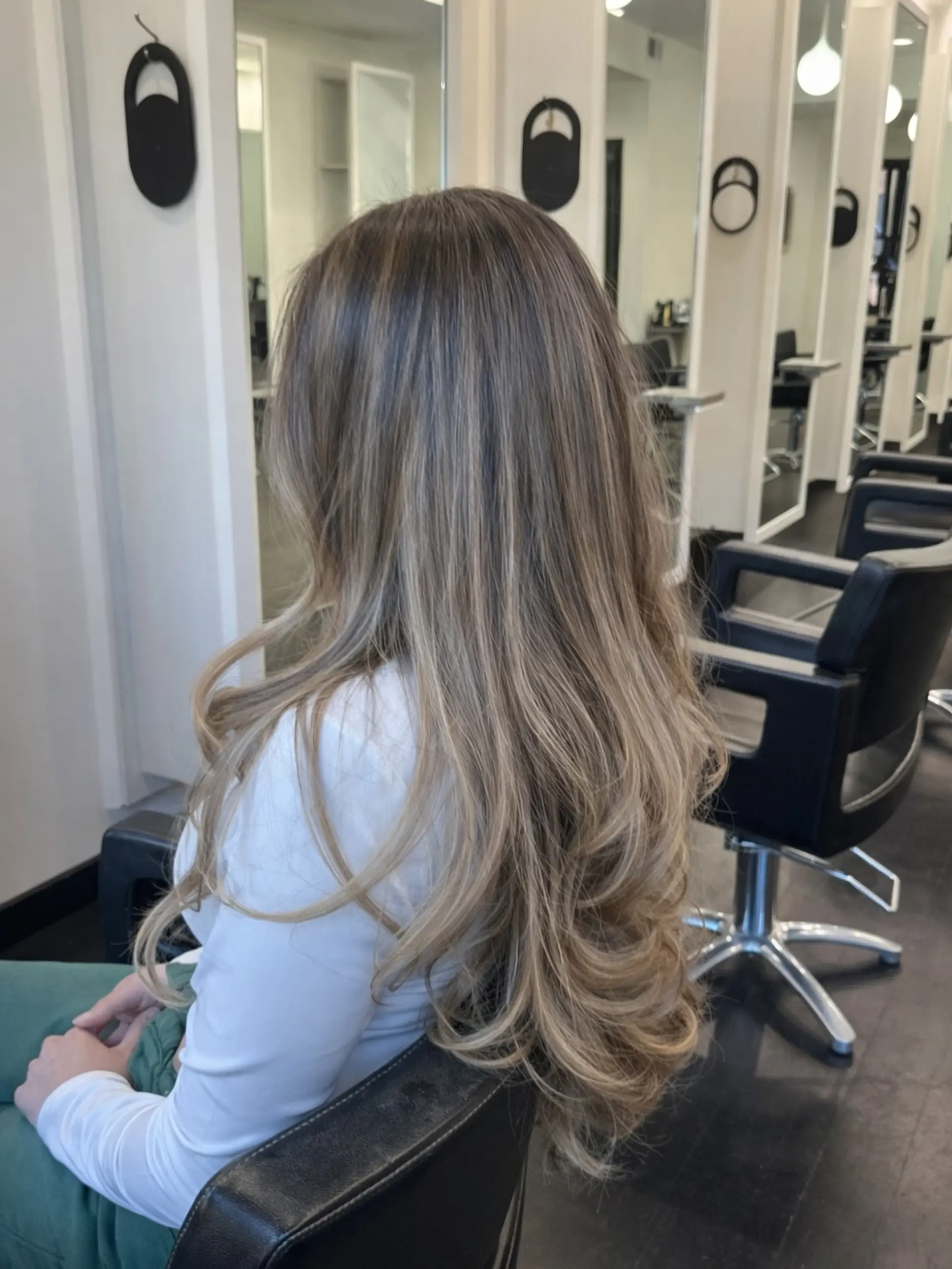 Extra-long layered hair styled with a seamless lived-in blonde balayage and soft, bouncy curved ends. 1
