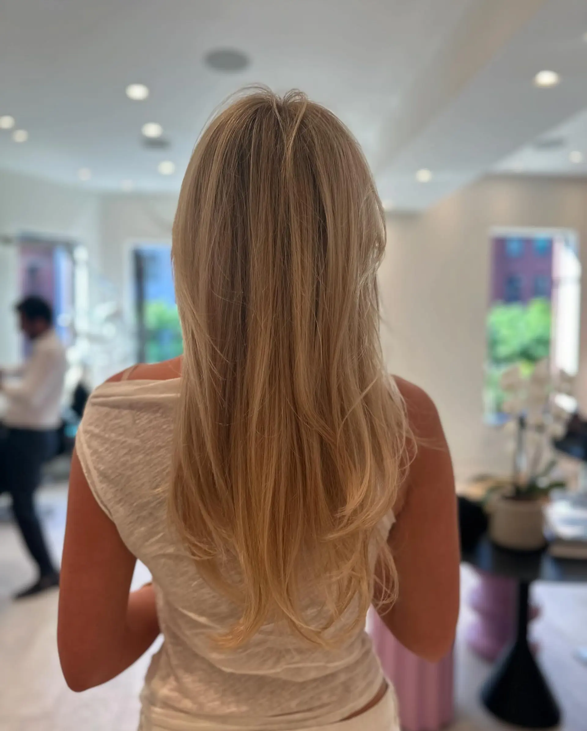 Long honey blonde hair cut with flowing layers and styled in a smooth, polished blowout with soft flipped ends. 1
