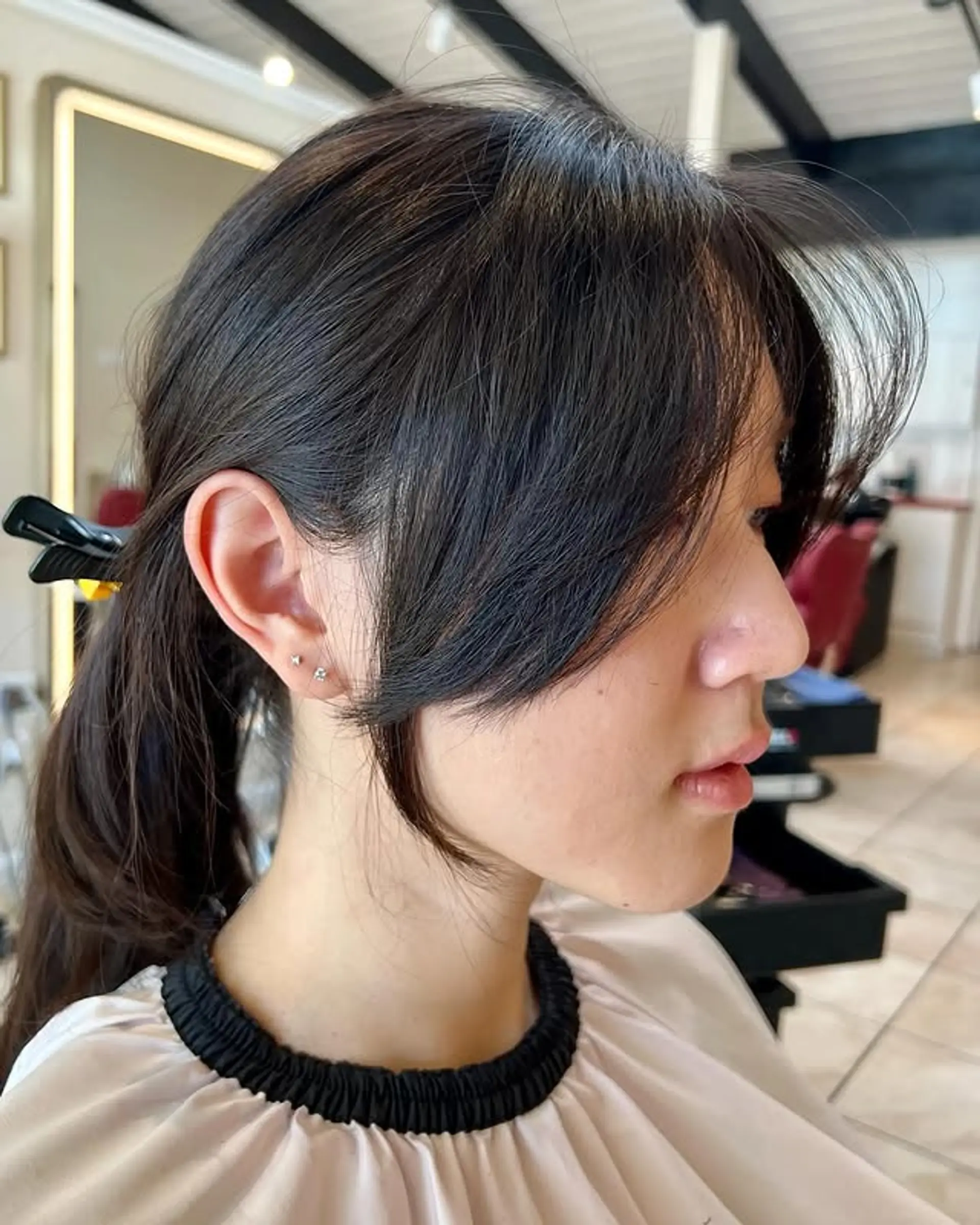 A chic layered cut with soft, face-framing curtain bangs that blend seamlessly into the rest of the hair, typically styled for an effortless and natural look, as seen here pulled back into a low ponytail. 1