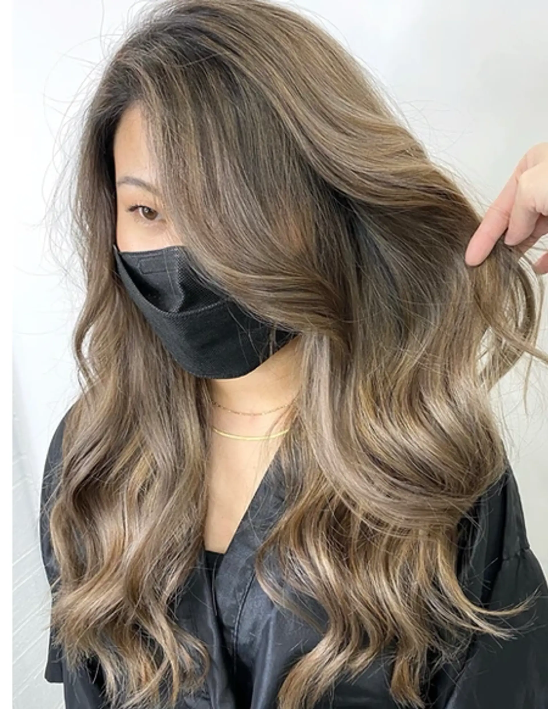 Long, wavy hair with ash blonde base color and light brown highlights. The style includes layered cuts and a side part for added volume and movement. 1