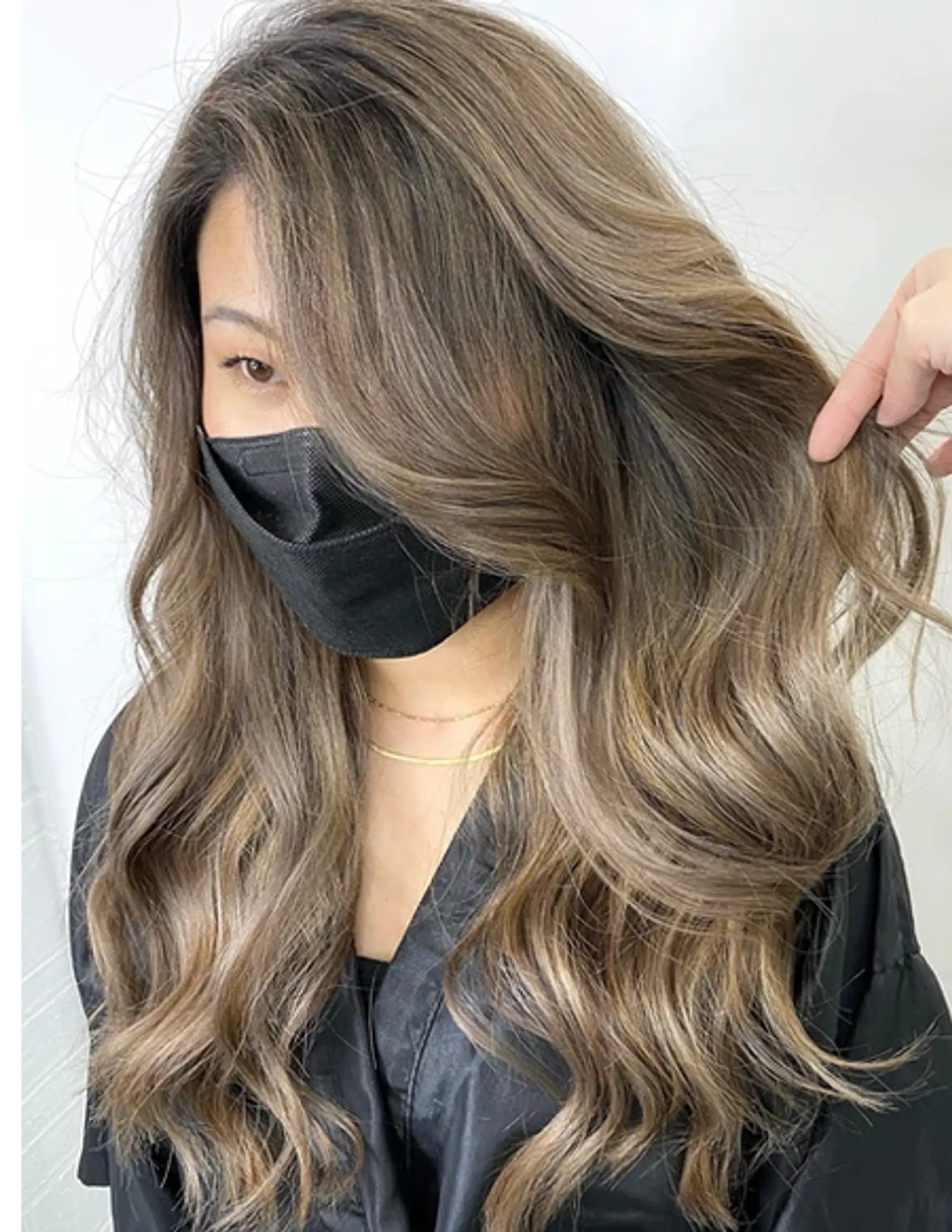 Long, wavy hair with ash blonde base color and light brown highlights. The style includes layered cuts and a side part for added volume and movement.