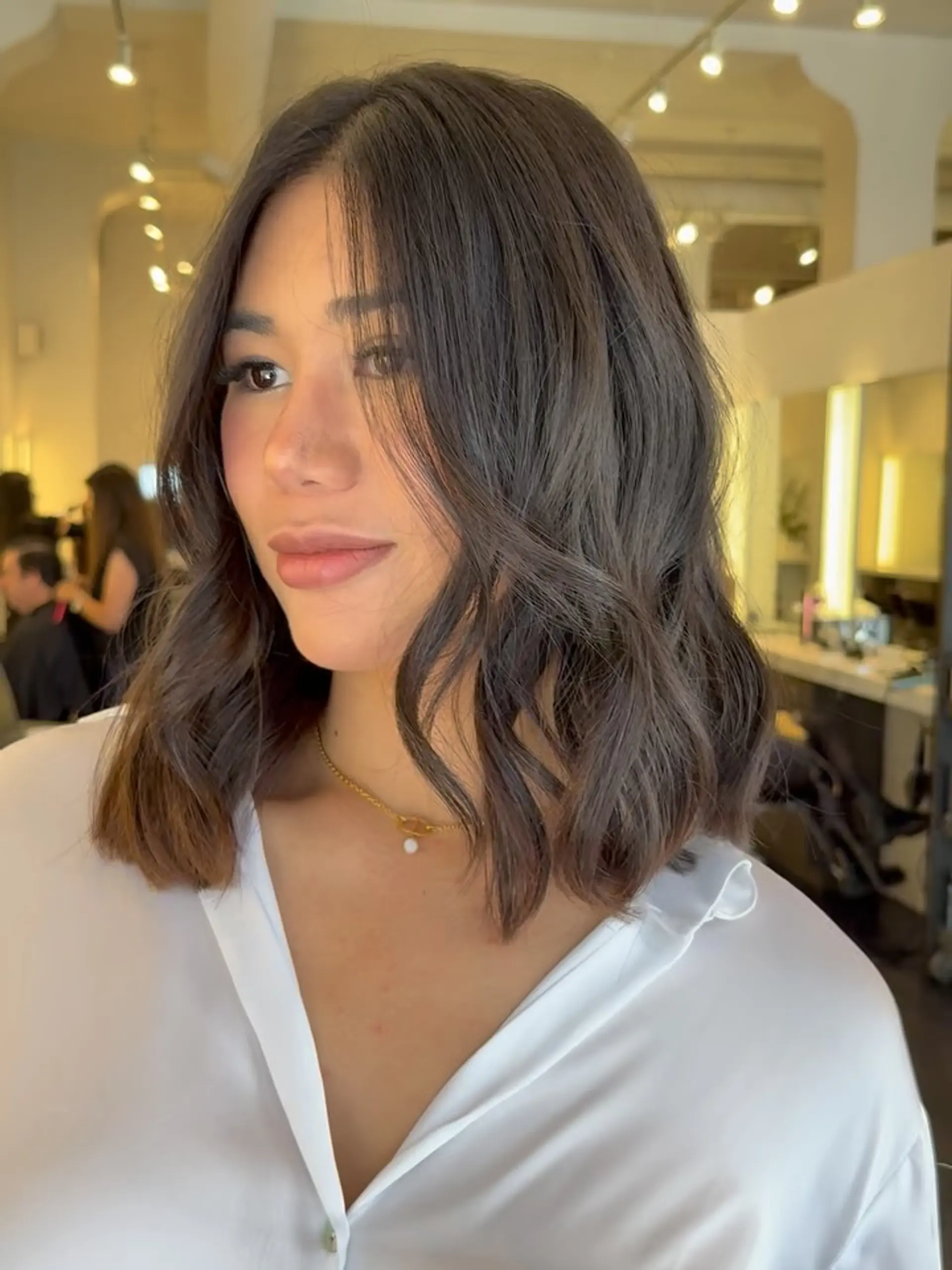 A collarbone-length brunette lob styled with soft, undone waves and gentle face-framing layers. 1