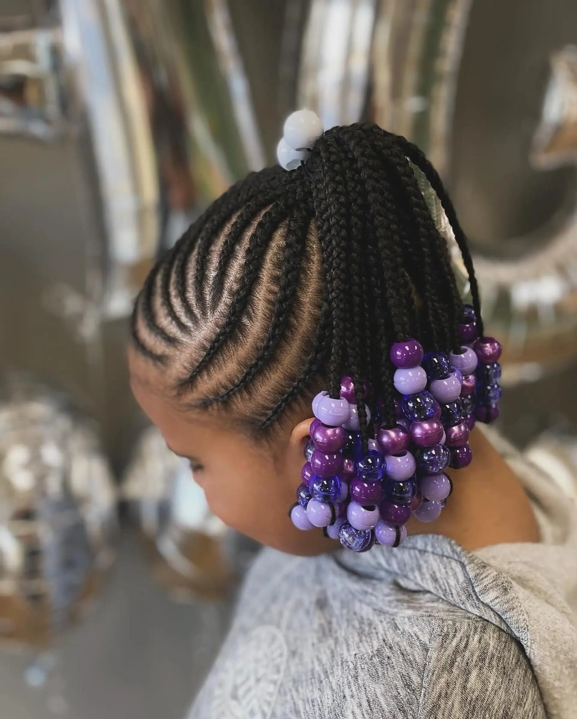 Precise curved cornrows gathered into a high braided ponytail accented with purple beads. 1