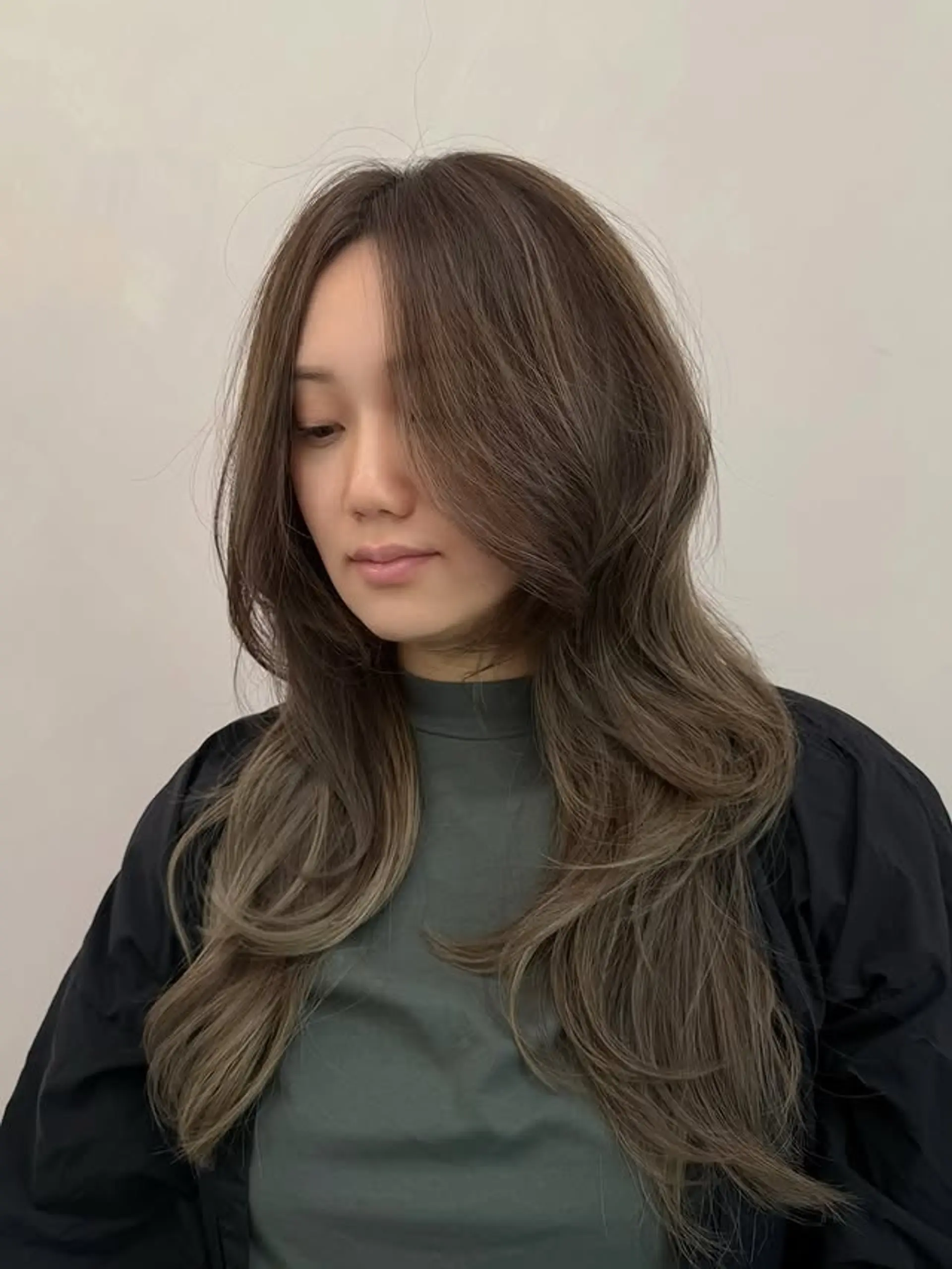 A long, layered haircut with soft face-framing pieces that mimic curtain bangs, adding volume and movement, especially when styled with subtle waves at the ends. 1