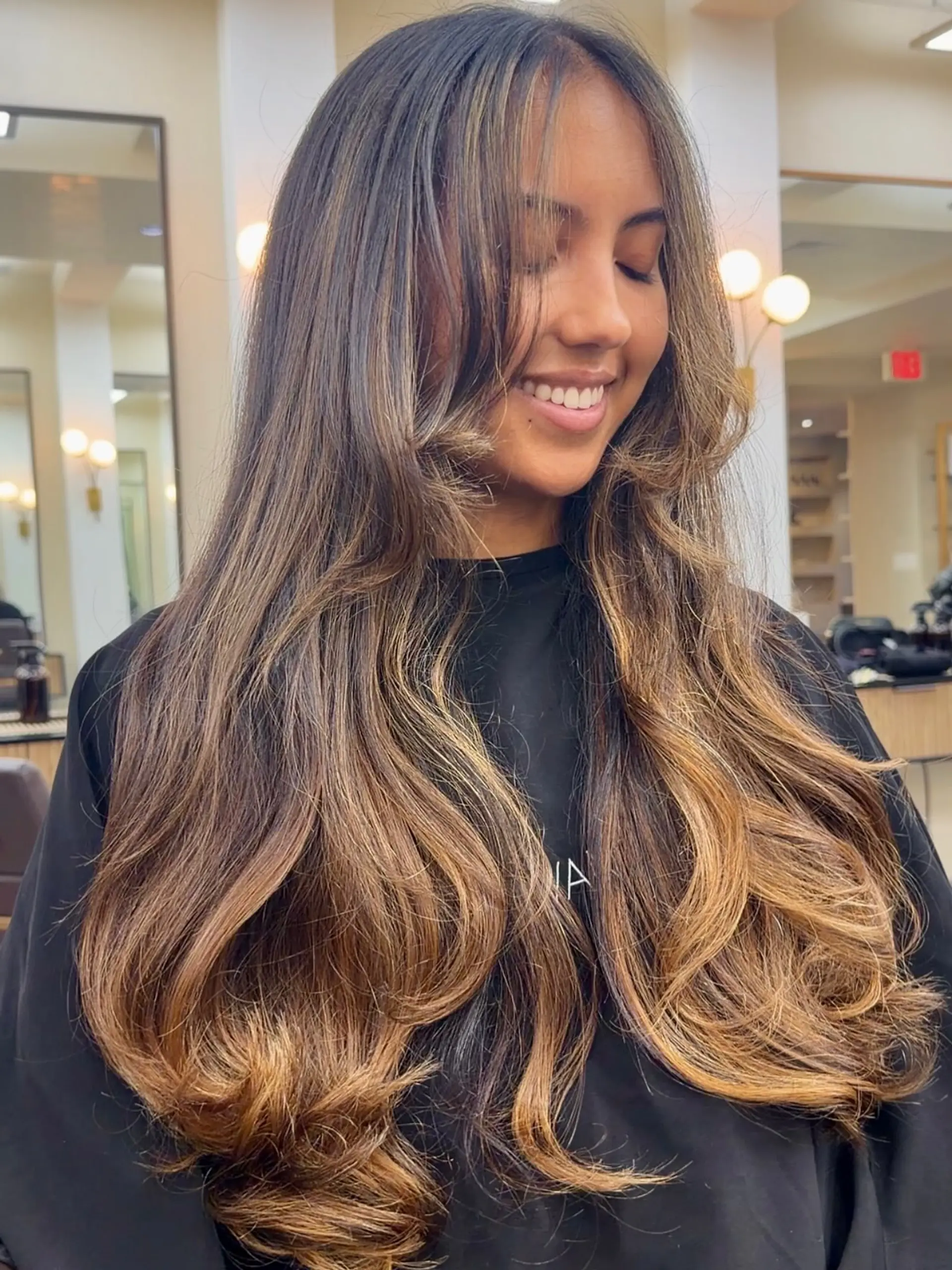 Extra-long hair styled in voluminous blowout waves featuring rich caramel balayage highlights and face-framing curtain layers. 1
