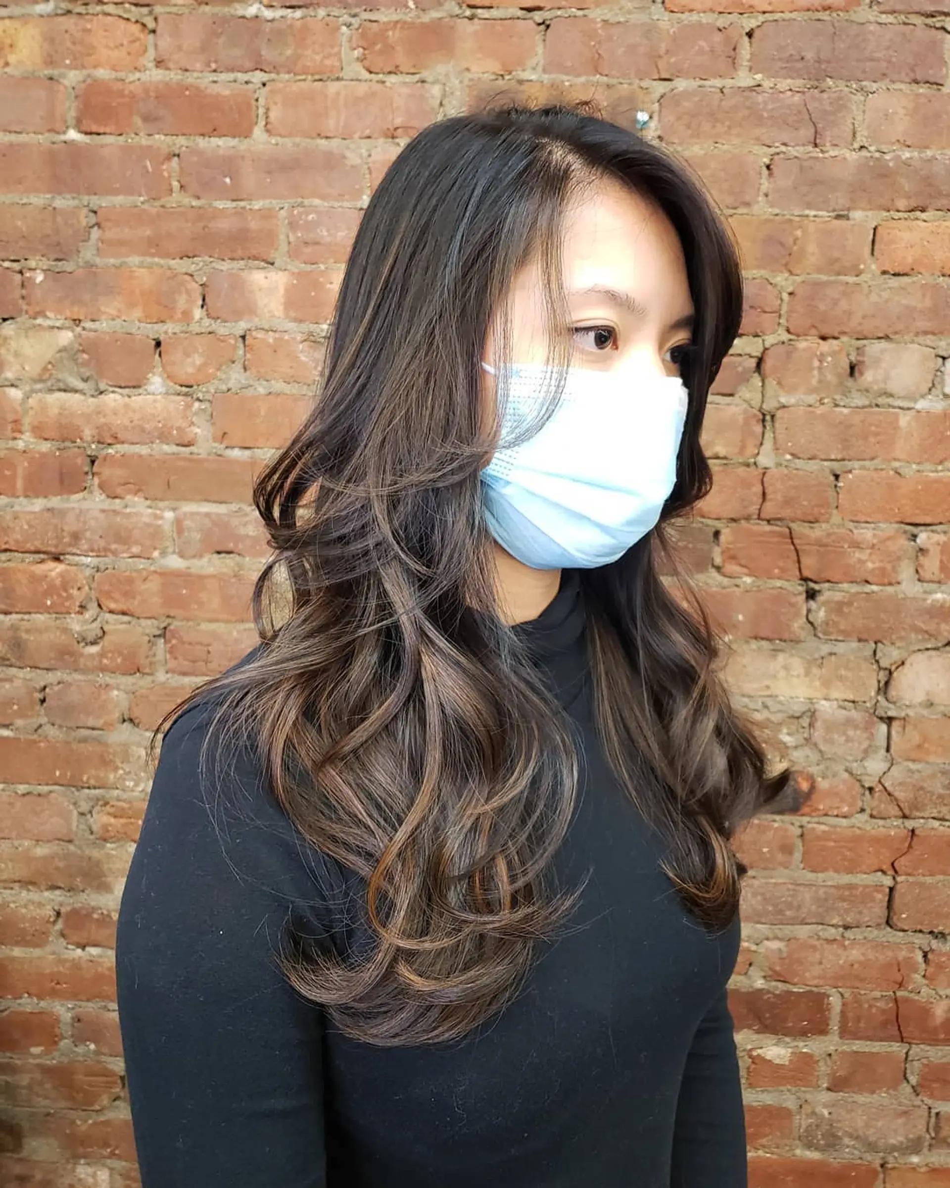 Long layered dark hair styled into voluminous, flowing curls with subtle warm brown balayage highlights. 1
