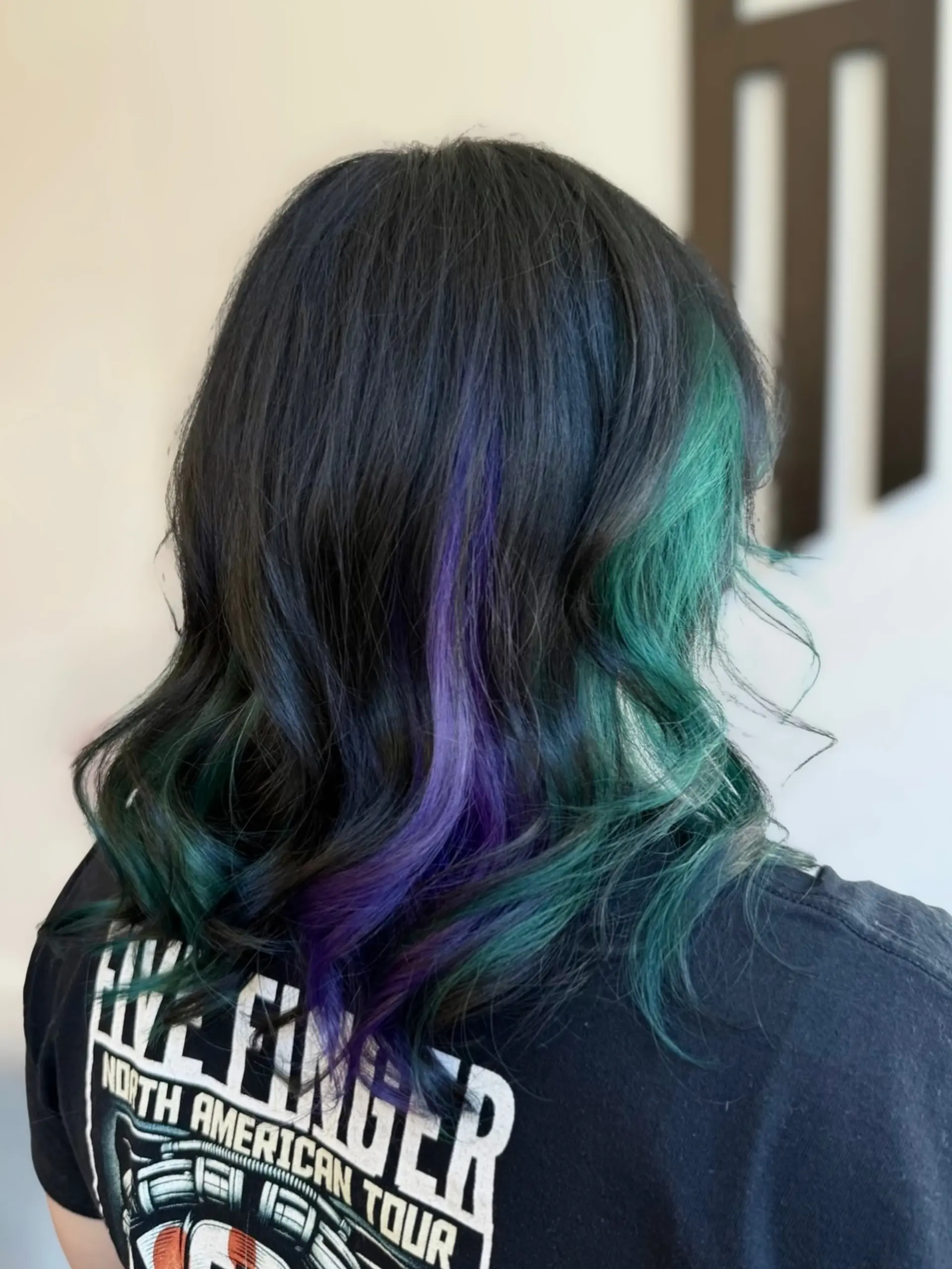 Medium-length wavy black hair featuring vivid purple and teal peekaboo highlights underneath. 1