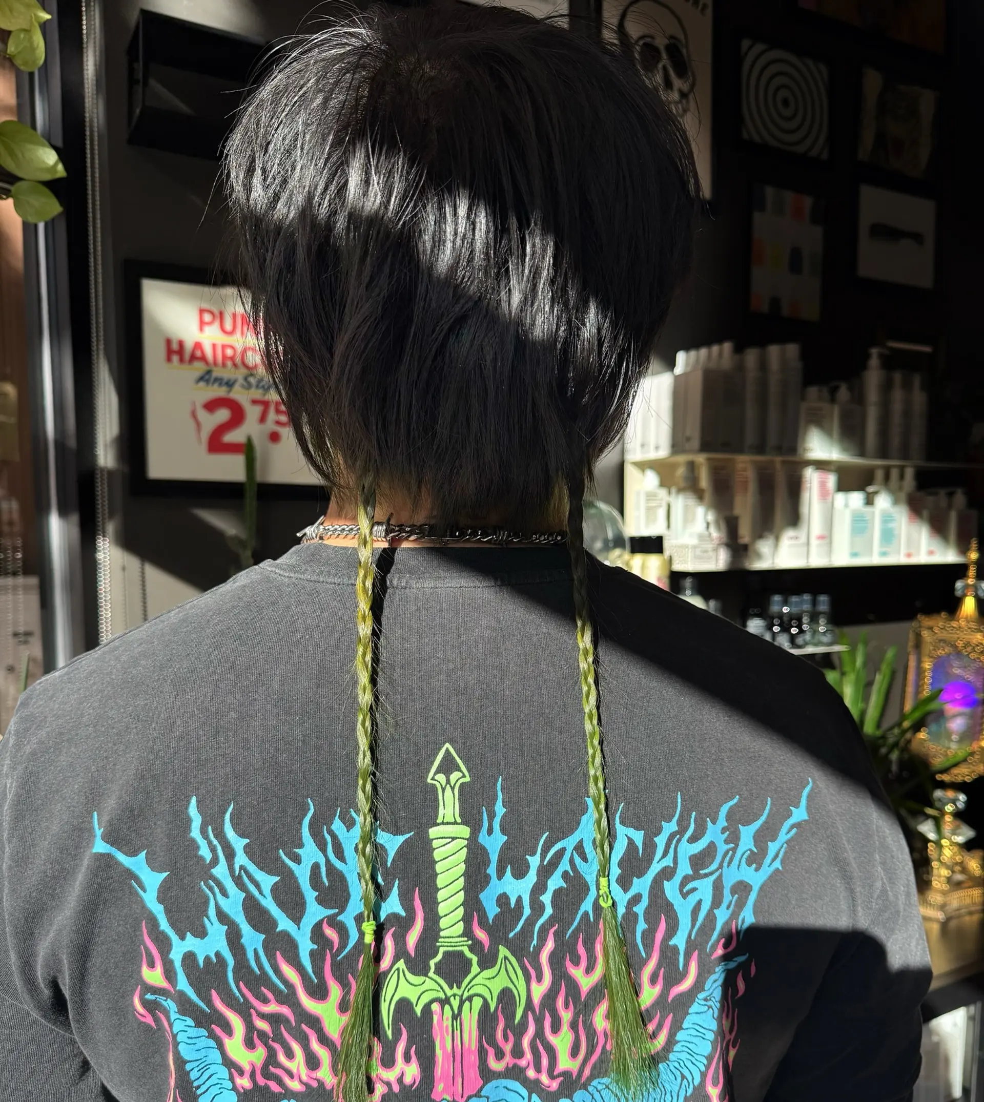 A textured short dark cut styled with two long, thin chartreuse green braided rat tails extending down the back. 1