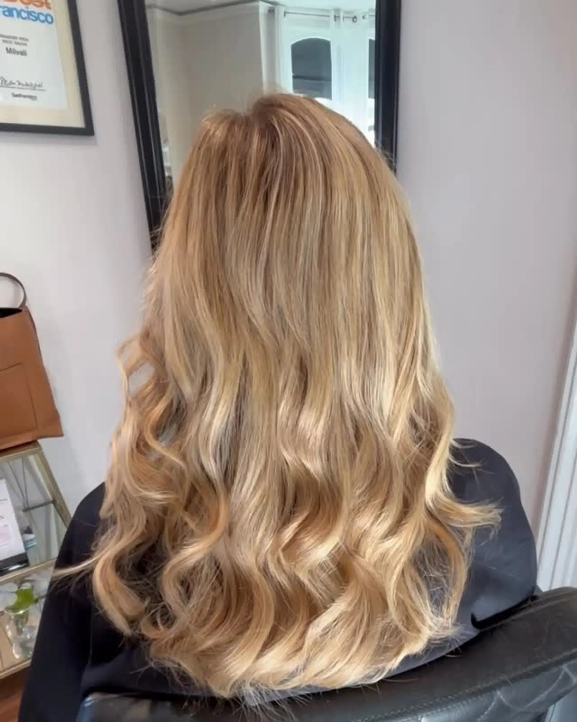 Long golden blonde hair styled in soft, voluminous waves, enhanced with seamless extensions for added thickness. 1