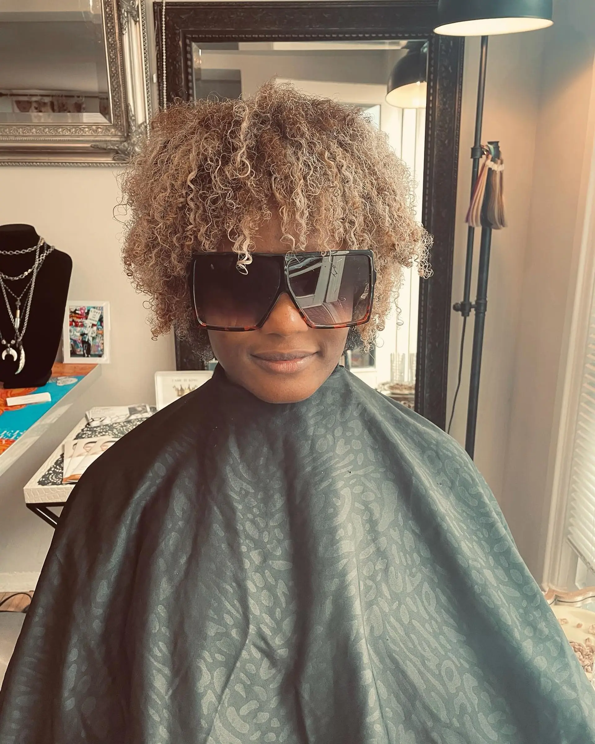A rounded, voluminous curly afro featuring dimensional beige blonde highlights paired with a natural dark shadow root. 1