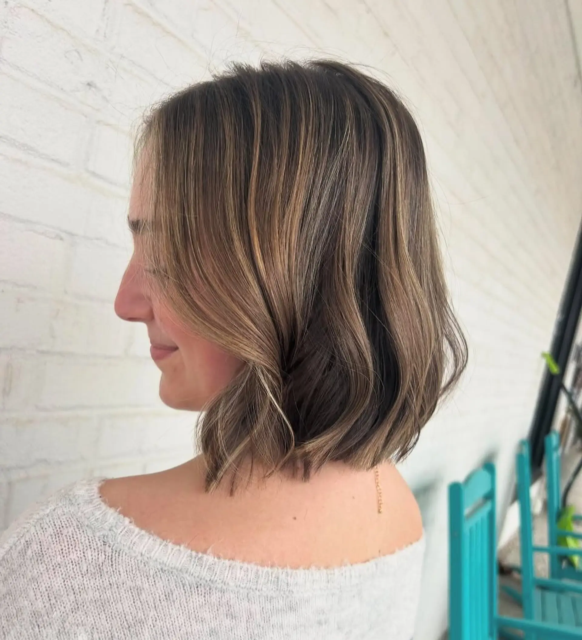 A blunt, textured neck-length bob styled with soft, undone waves and dimensional lived-in blonde highlights. 1