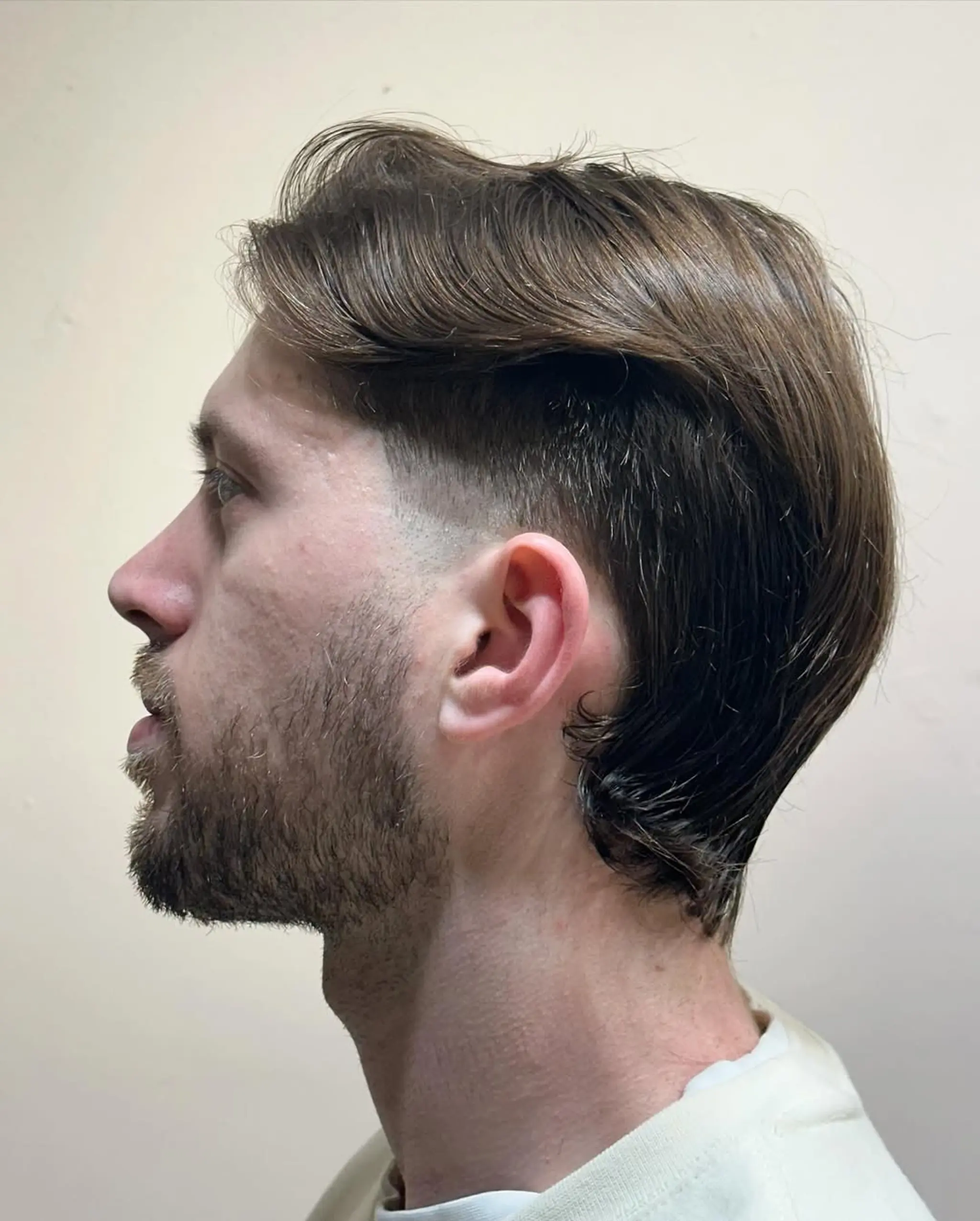 Medium-length wavy brown hair styled with a smooth side part and gentle wave. The sides are tapered into a fade, with the lengthier top section swept back and tucked behind the ear. 1