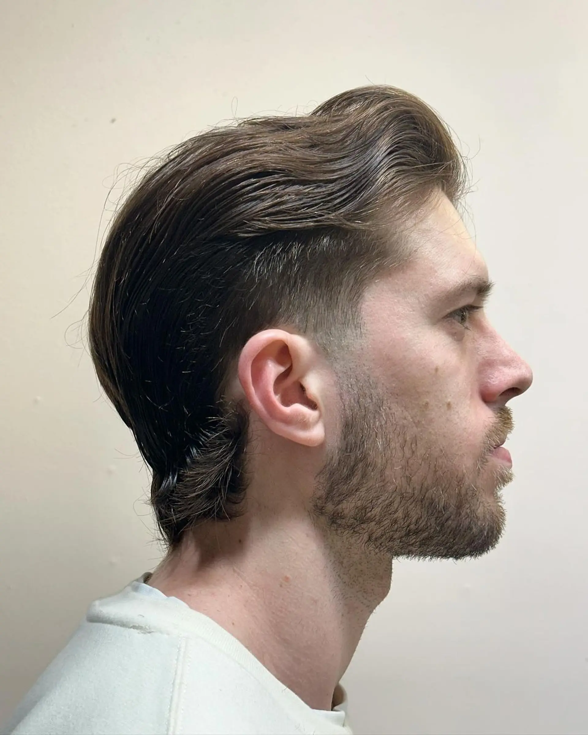 Medium-length wavy brown hair styled with a smooth side part and gentle wave. The sides are tapered into a fade, with the lengthier top section swept back and tucked behind the ear. 2
