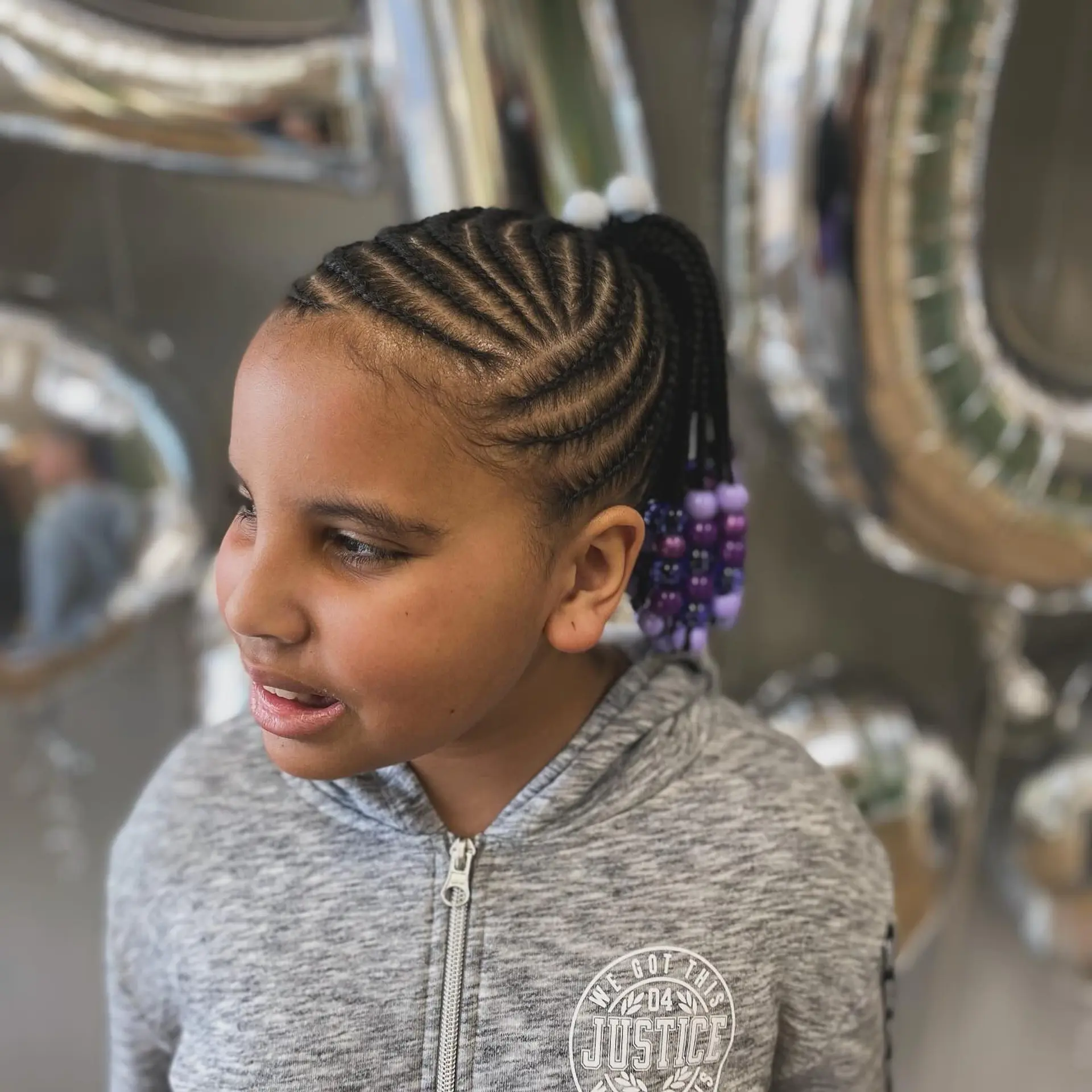 Neat cornrows braided upward into a high ponytail adorned with purple and white beads. 1