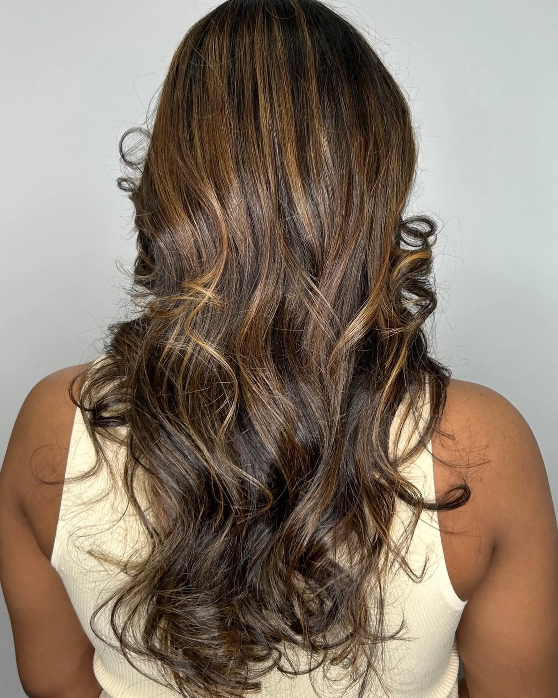 Long layered brunette hair with dimensional caramel balayage styled in loose curls and waves. 1