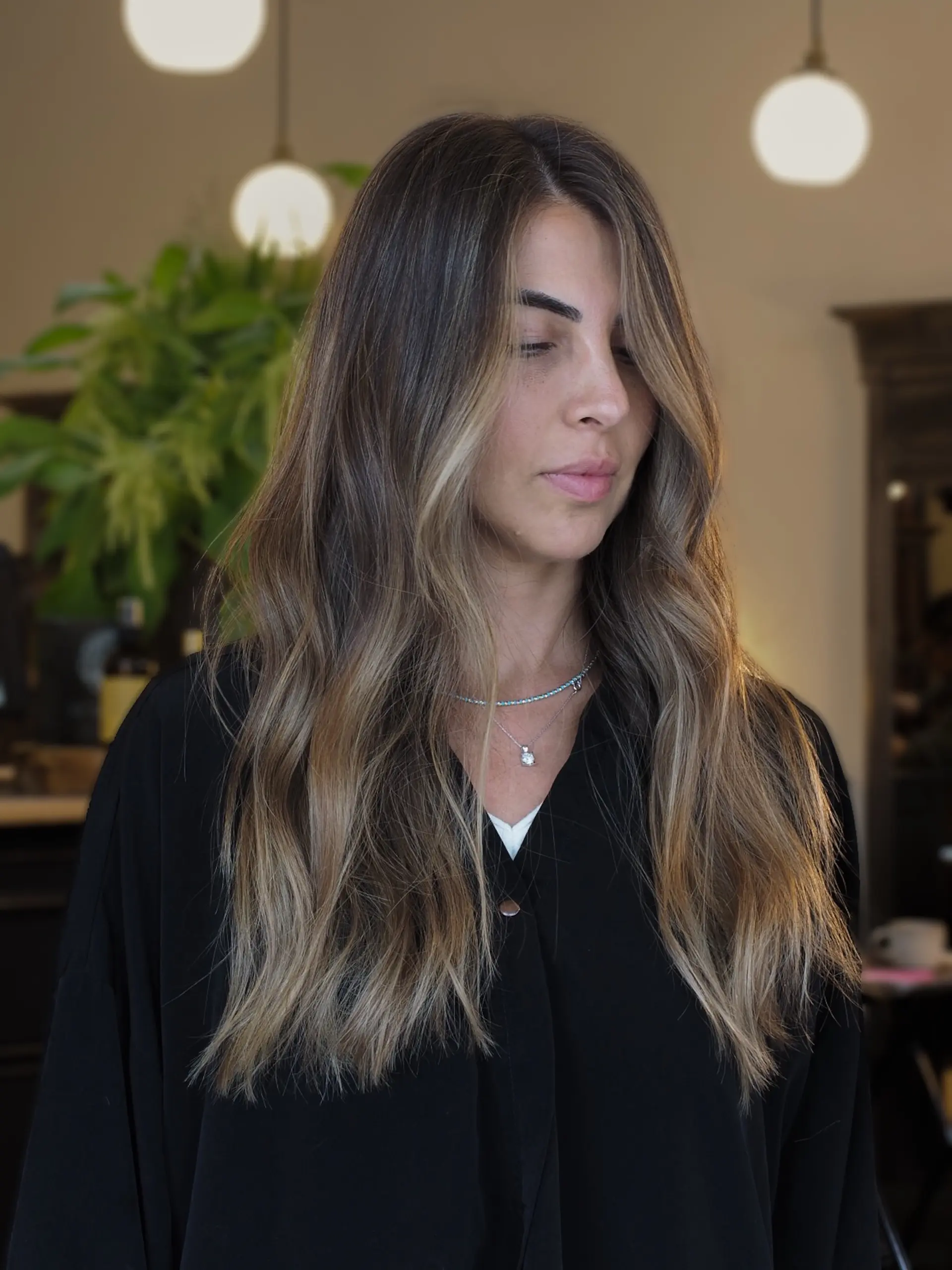Long wavy brunette hair illuminated with subtle golden blonde highlights and soft face-framing pieces. 1