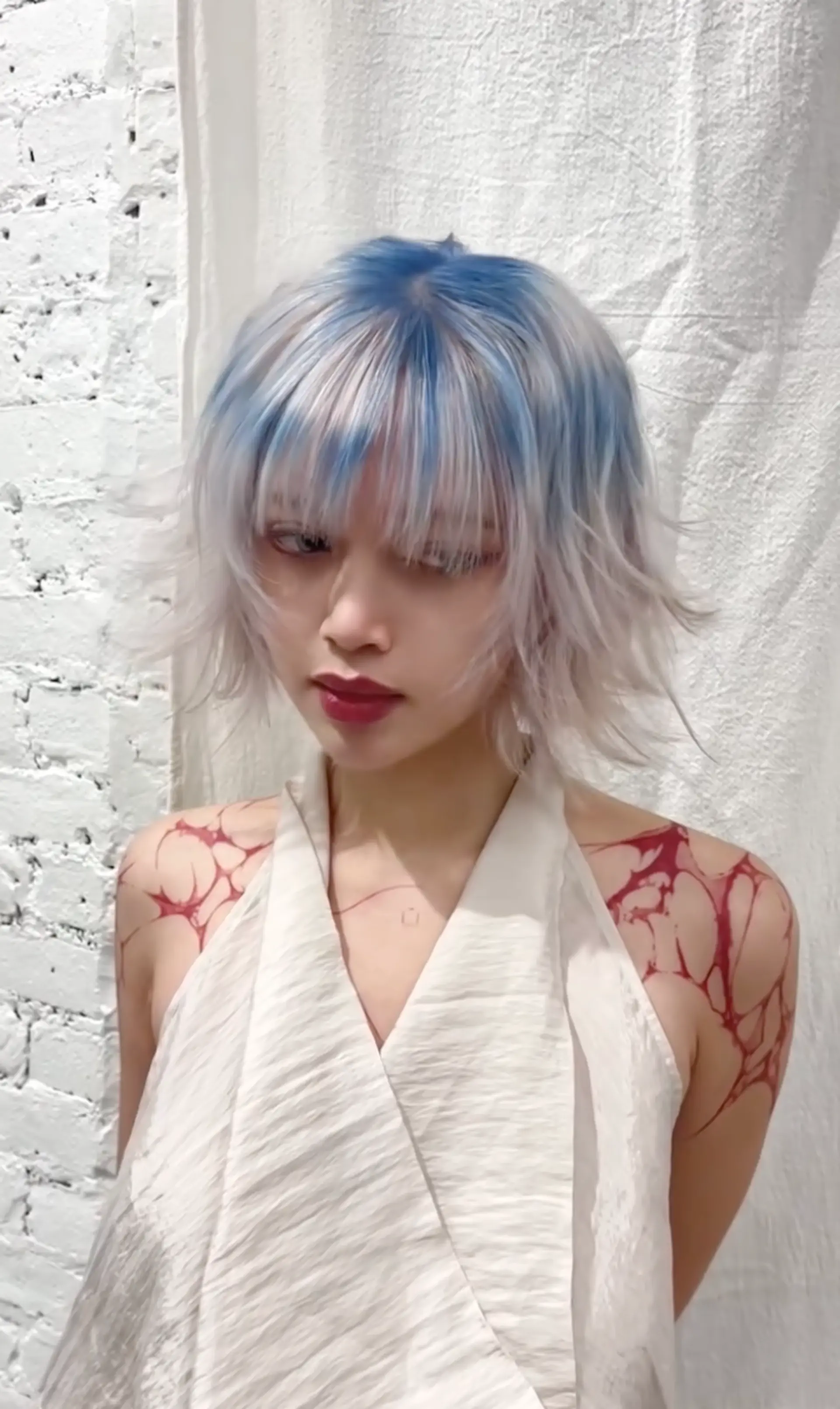 A short, wavy hairstyle featuring platinum blonde with vivid blue highlights. It includes shaggy layers, textured ends, and a choppy fringe for a tousled and edgy look. 1