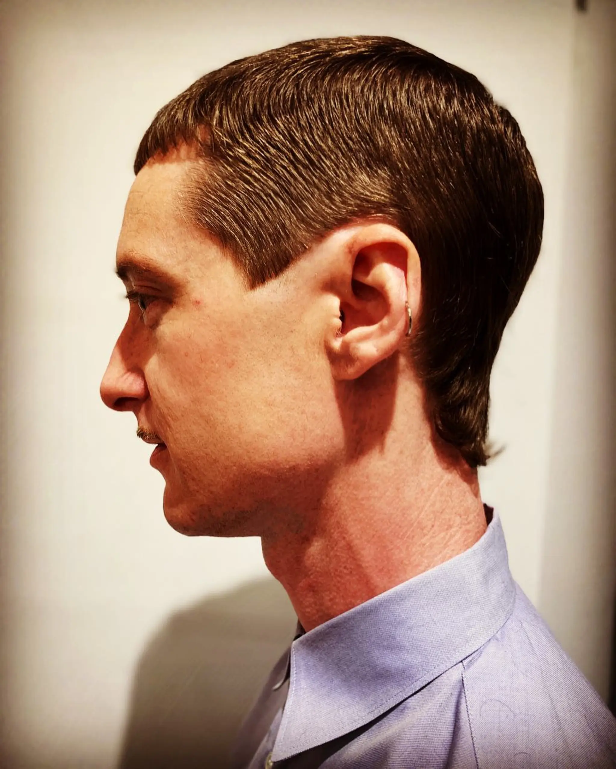 A sleek, straight hairstyle featuring precise tapering with a clean finish and a subtle wave, complemented by an ear-length mullet.