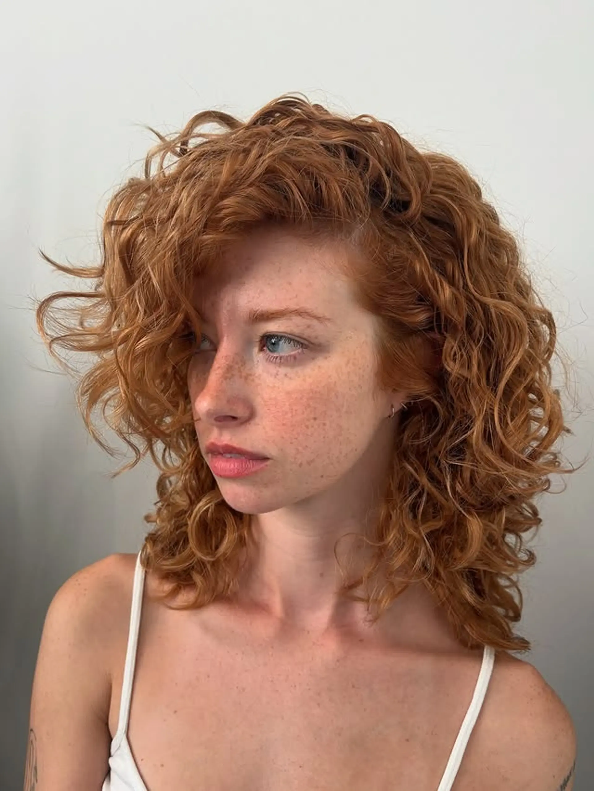 A trendy medium-length haircut featuring voluminous copper-red curls and flattering layers. 1