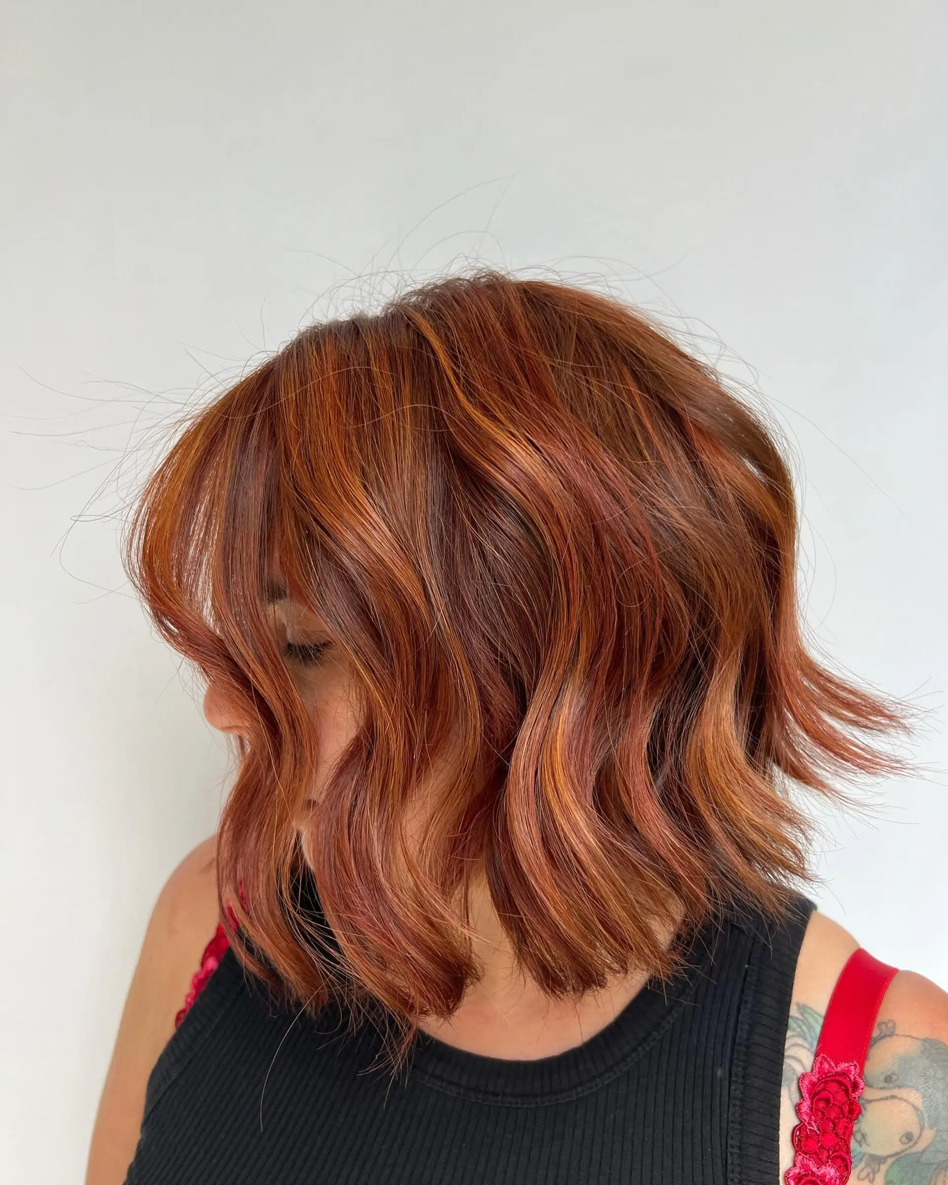 A textured chin-to-neck length wavy bob colored in rich copper and warm brown ribbon highlights. 1