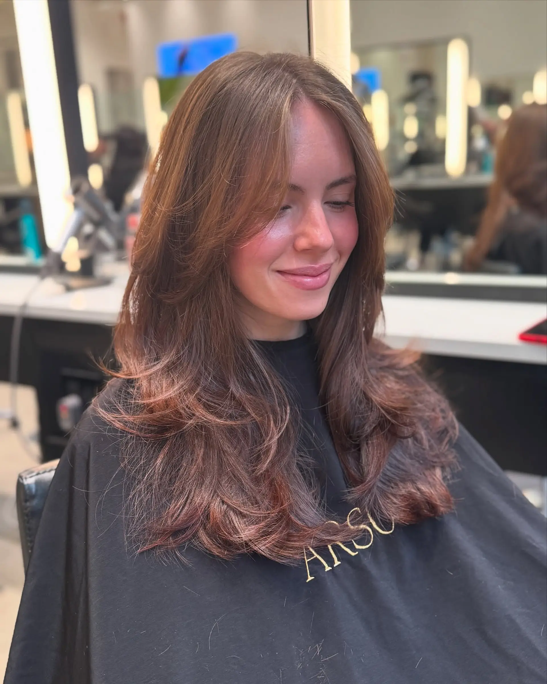 A medium-length, layered haircut with face-framing layers and a smooth blowout finish. 2
