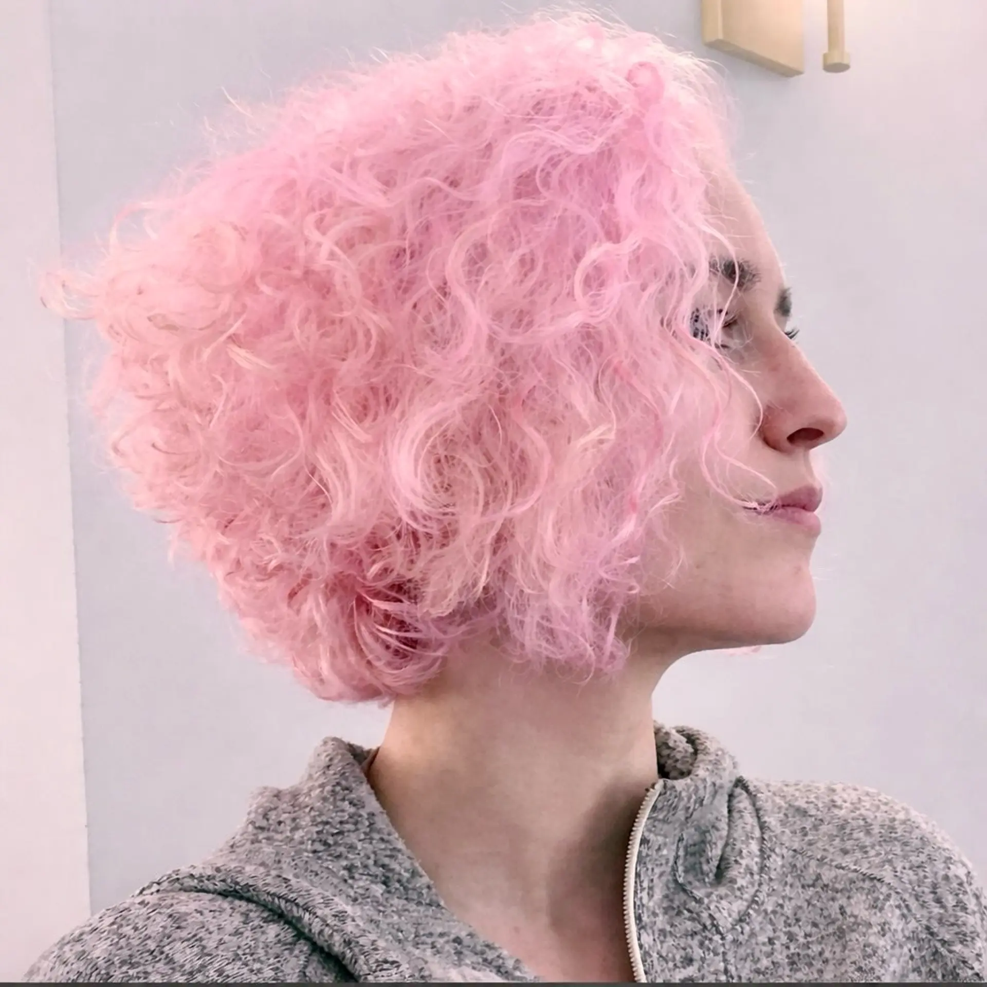 A voluminous, chin-length curly bob colored in a soft quartz pastel pink. 1