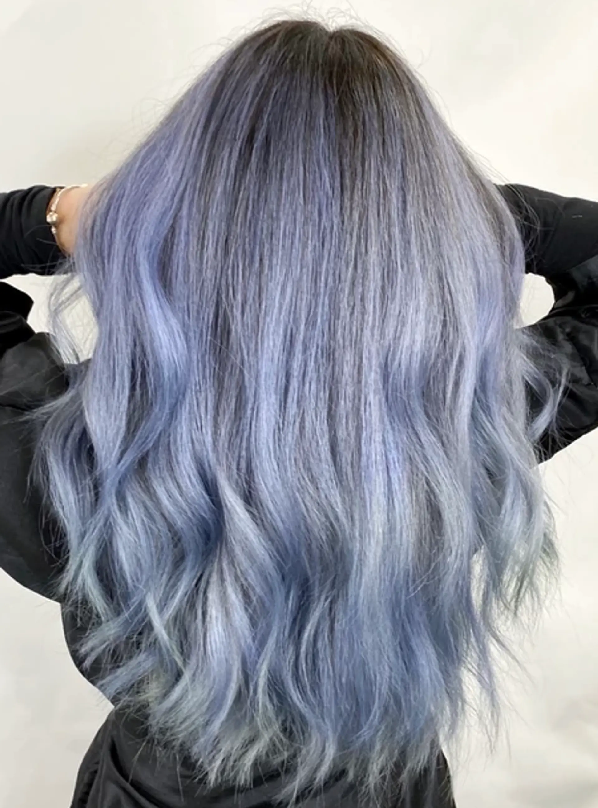 An exquisite long wave hairstyle with predominantly silver hair featuring hints of lavender and blue. The hair flows down gracefully in soft, cascading waves, with a striking ombre effect, transitioning from darker roots to lighter hues. The wavy texture adds volume and movement, making the style bold and elegant. 1