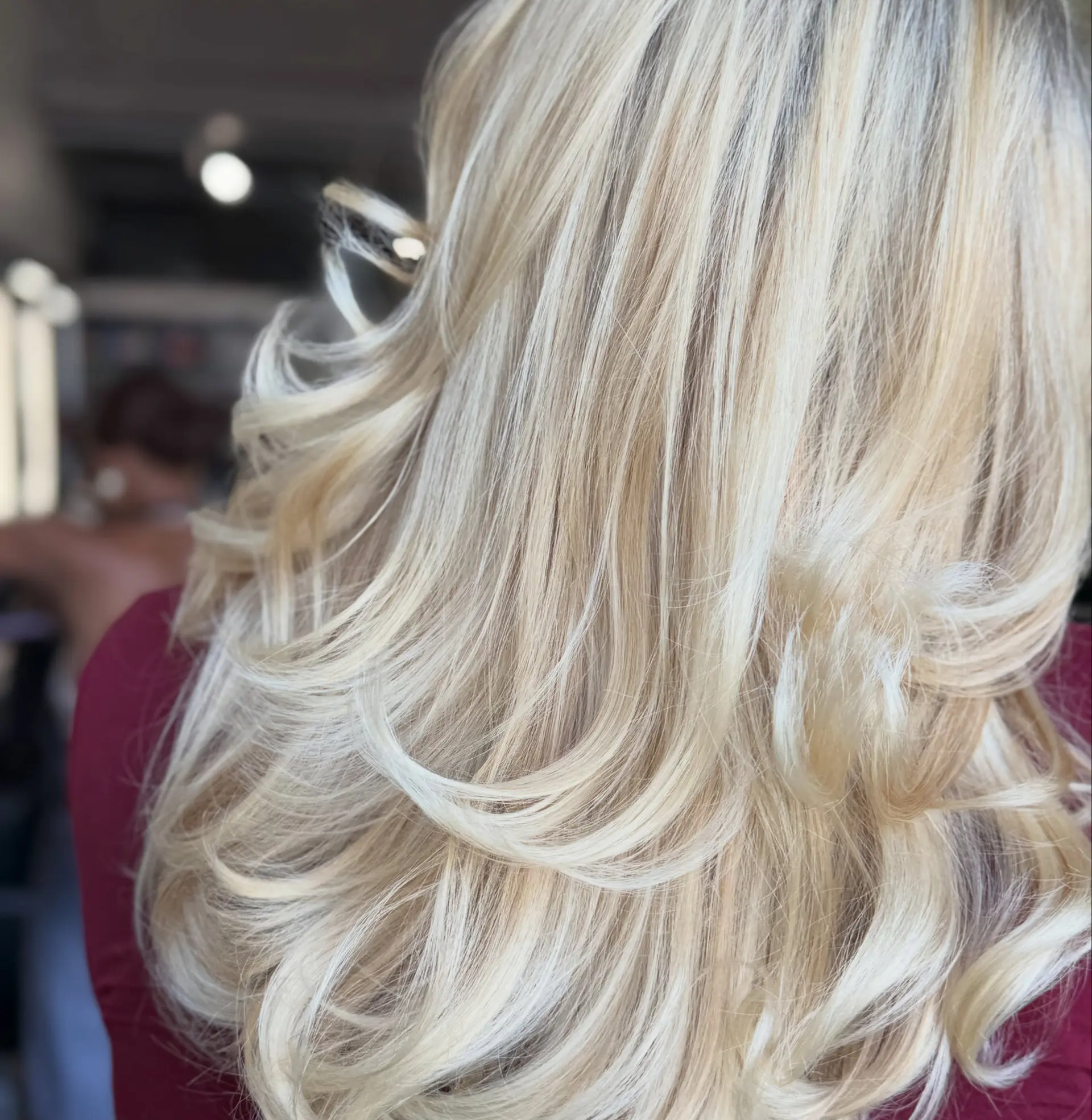 A bouncy, high-volume blowout on long, layered light blonde hair with curled, flicked ends. 1