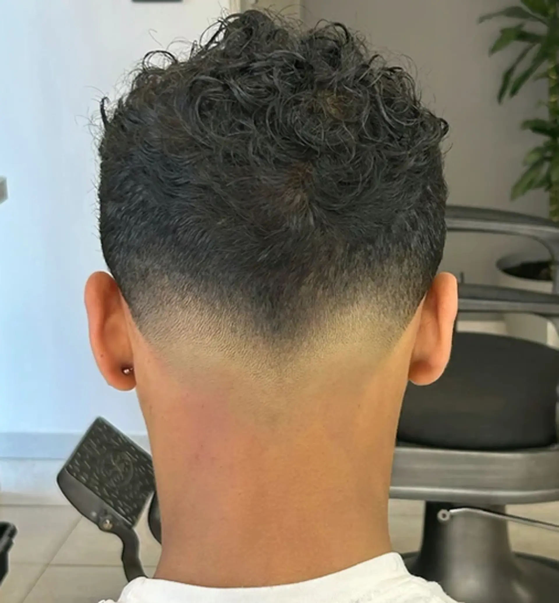 Curly hairstyle with a short length featuring a tapered fade. Defined curls on top create a bold texture contrast with the gradual fade along the sides. 1