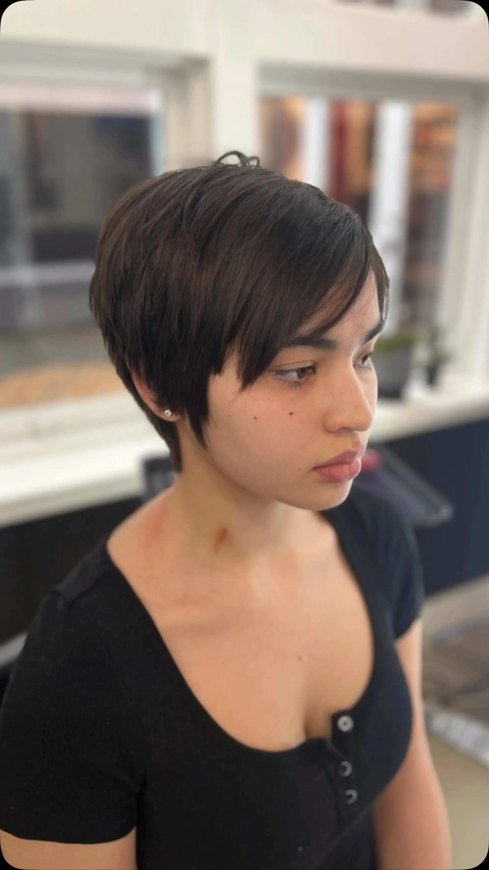 A sleek, short pixie cut in deep dark brown featuring soft, side-swept fringe and tapered sides. 1