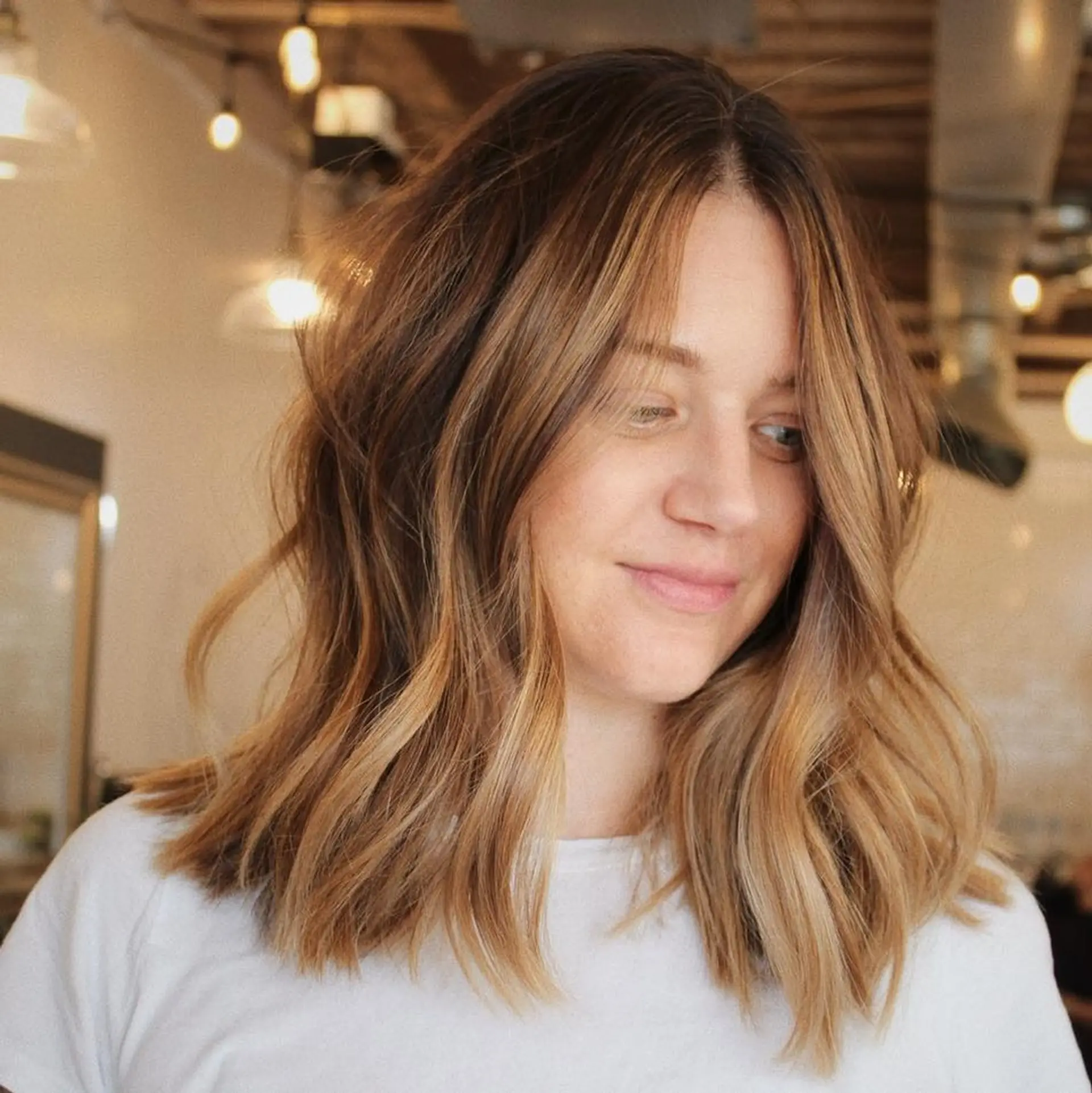 A textured shoulder-length lob featuring warm caramel and honey blonde reverse balayage dimension, styled with relaxed, effortless waves. 1