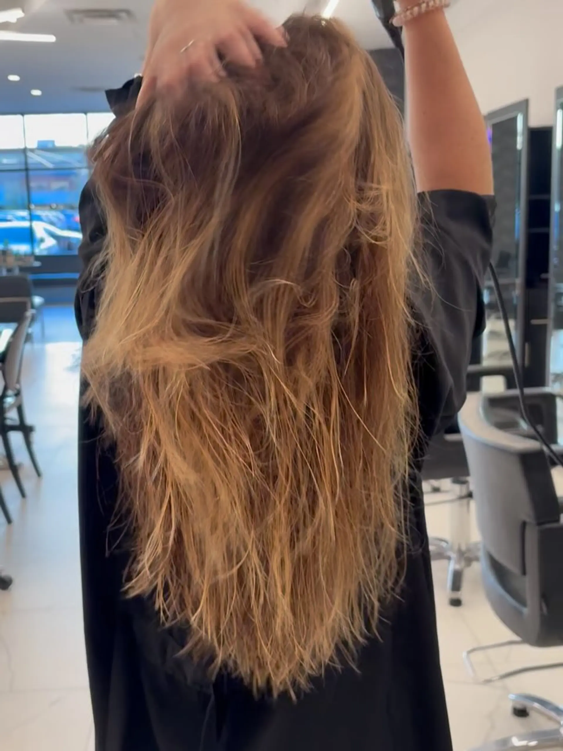 Long layered hair featuring warm dimensional blonde highlights styled into effortless, textured beach waves. 1