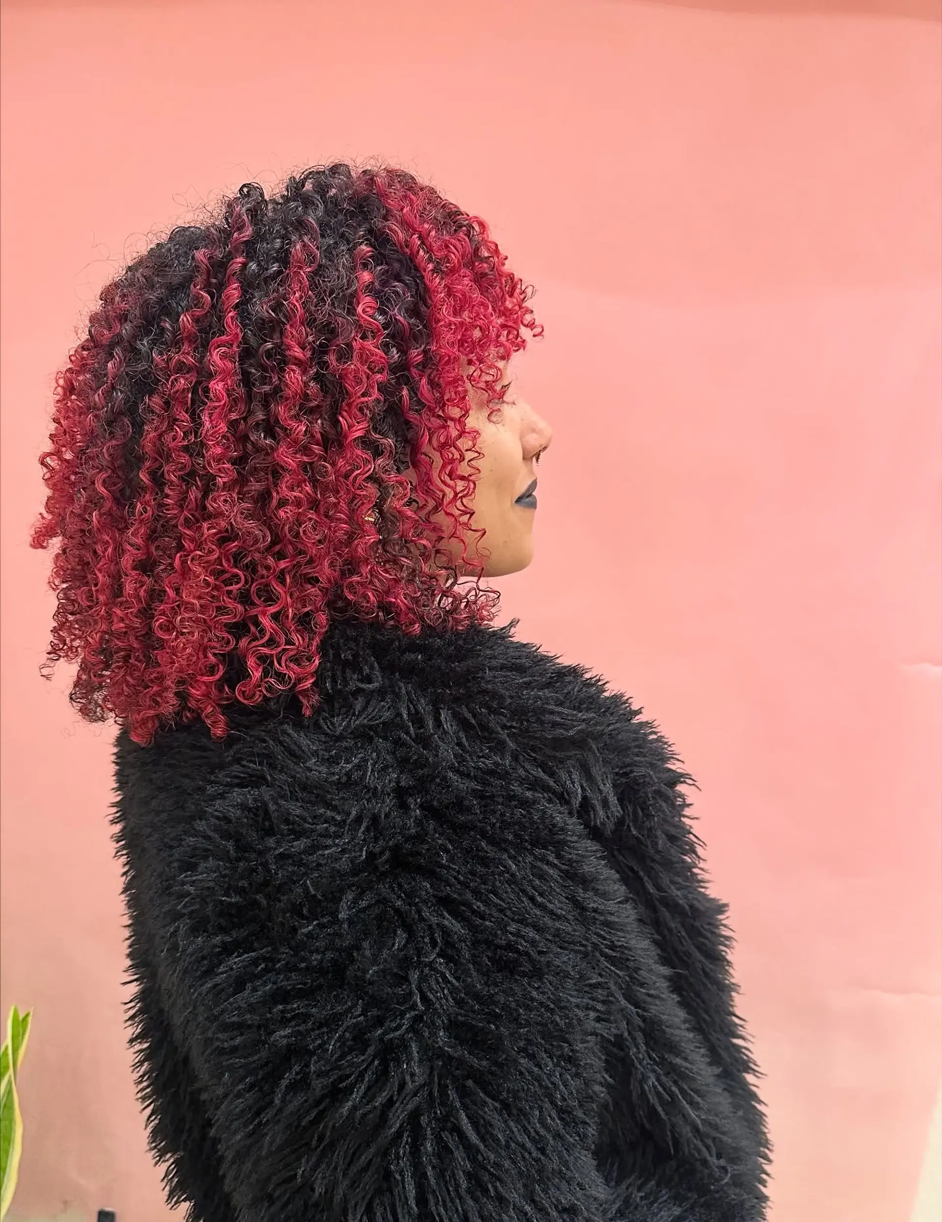 Shoulder-length, tight curly cut with a rounded shape, curly bangs, and vibrant magenta-red balayage highlights. 1