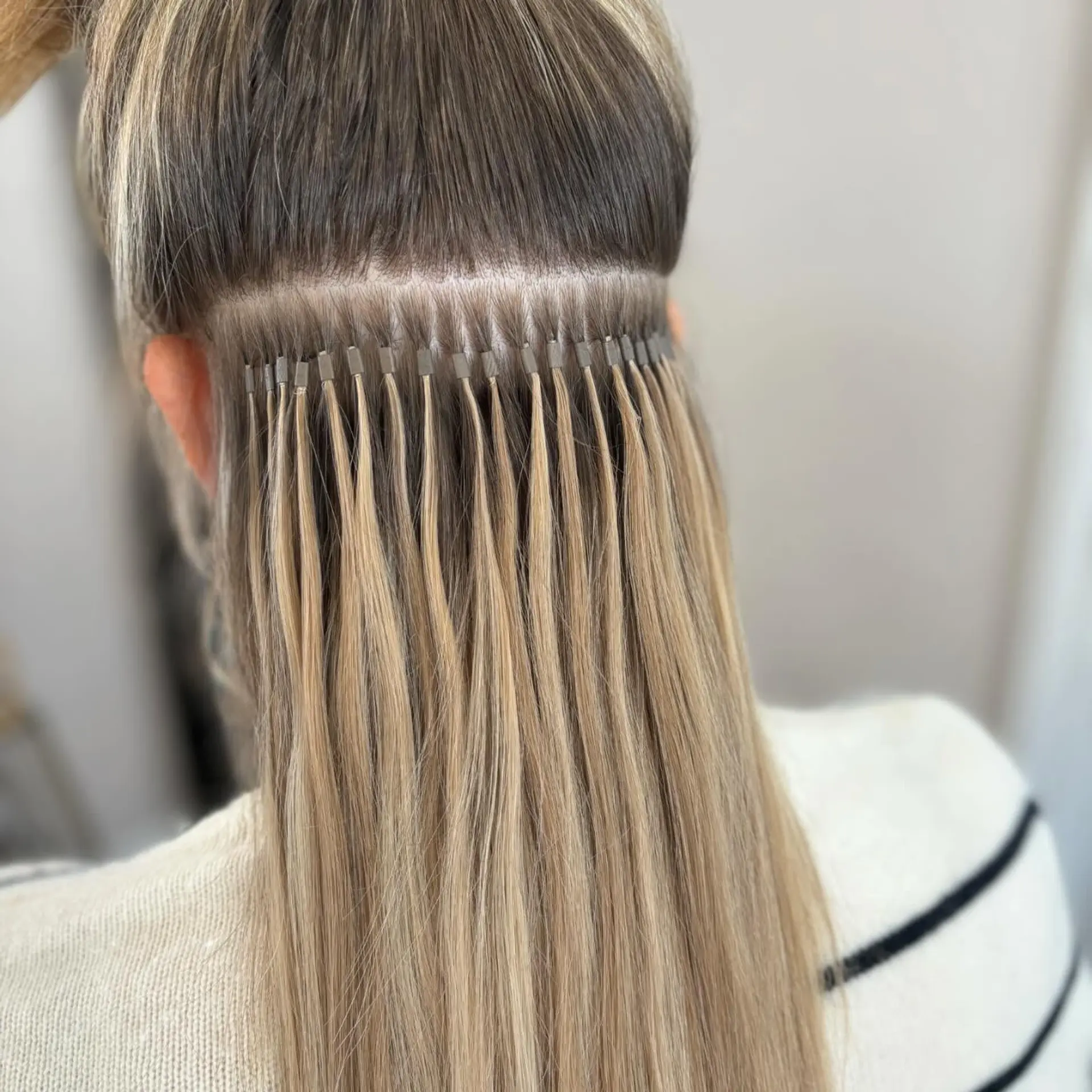 A precise row of blonde I-tip extensions installed beneath natural light brown hair to add length, volume, and chemical-free highlights. 1