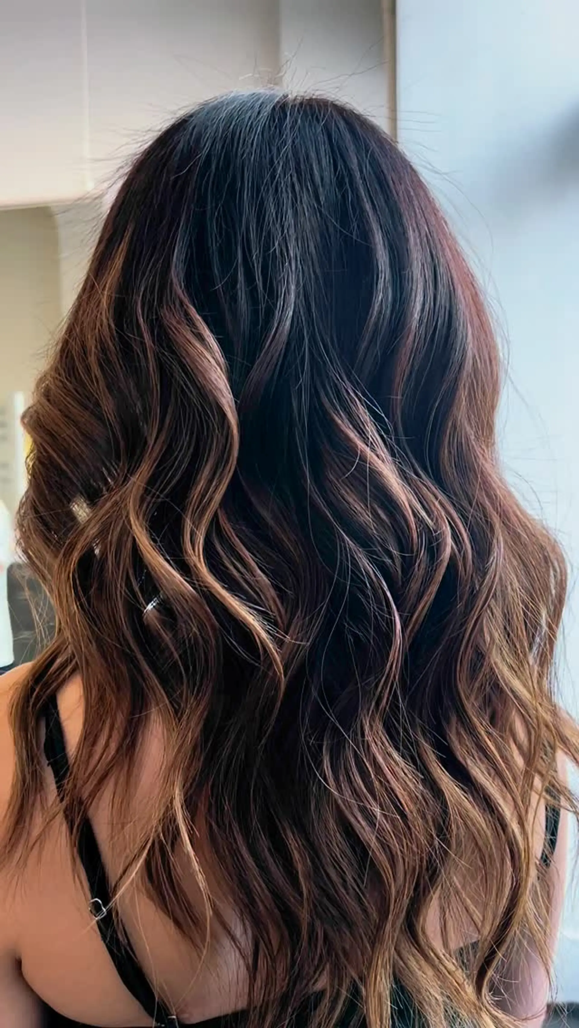 Long deep brunette hair accentuated with warm caramel balayage highlights and styled into loose waves. 1