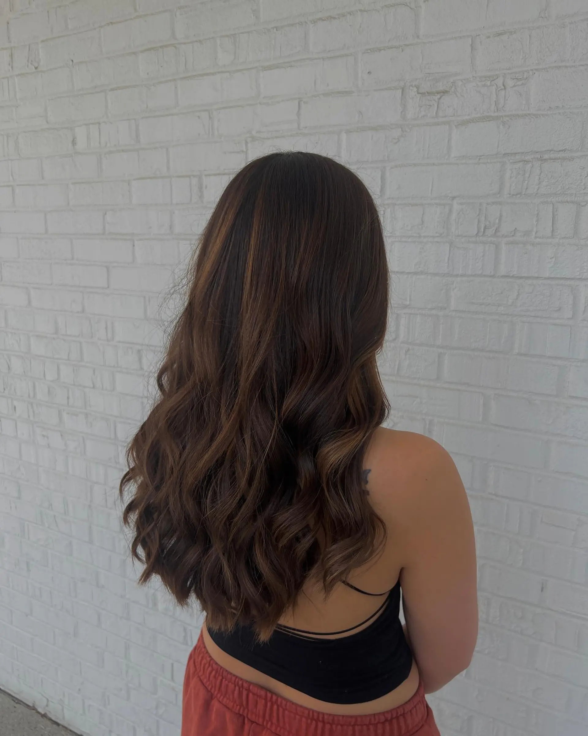Long chocolate brunette hair featuring soft, natural warm balayage highlights styled in loose waves. 1