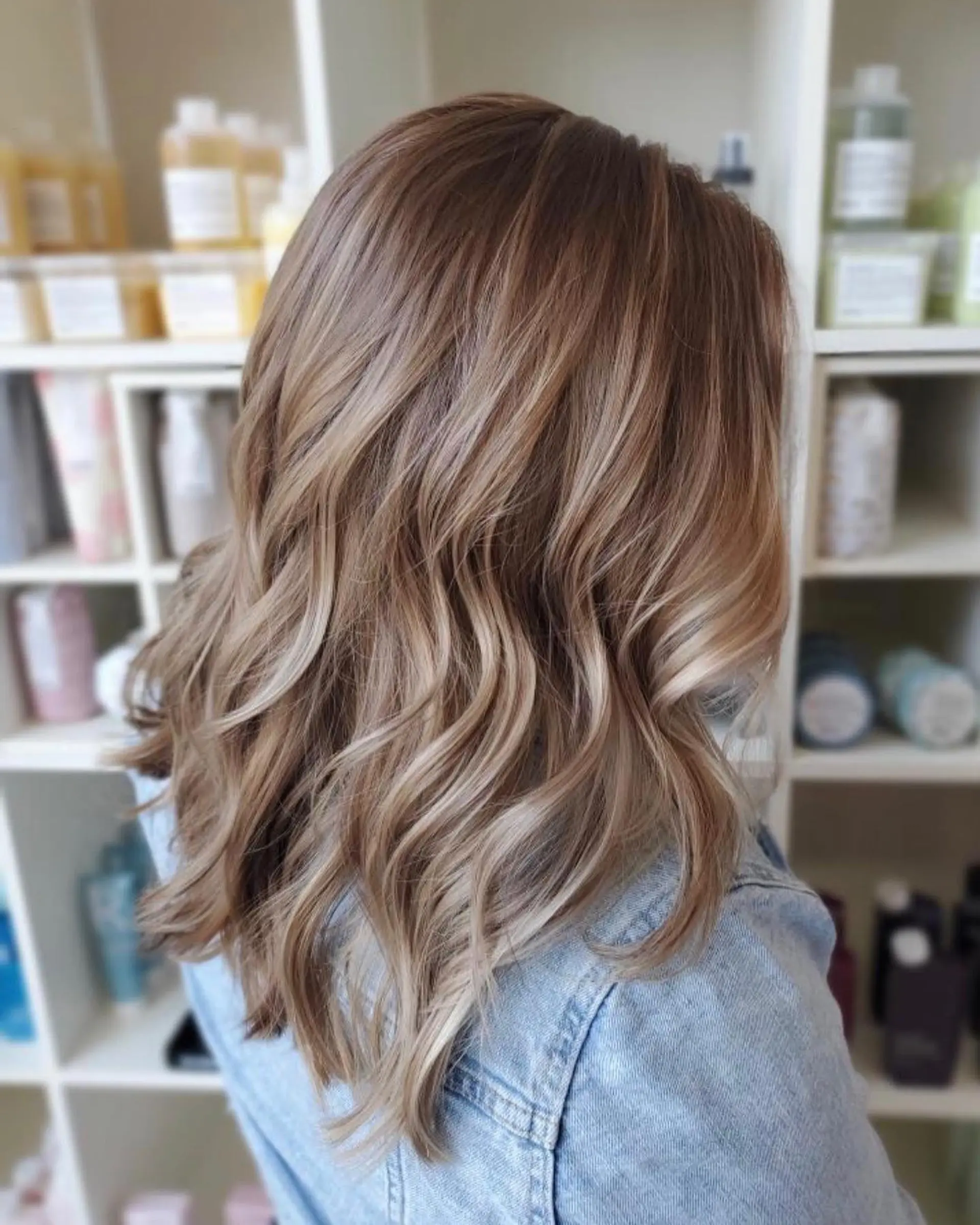 Medium-length wavy hair with a seamless color melt transitioning from a natural brunette root into blended blonde highlights. 1
