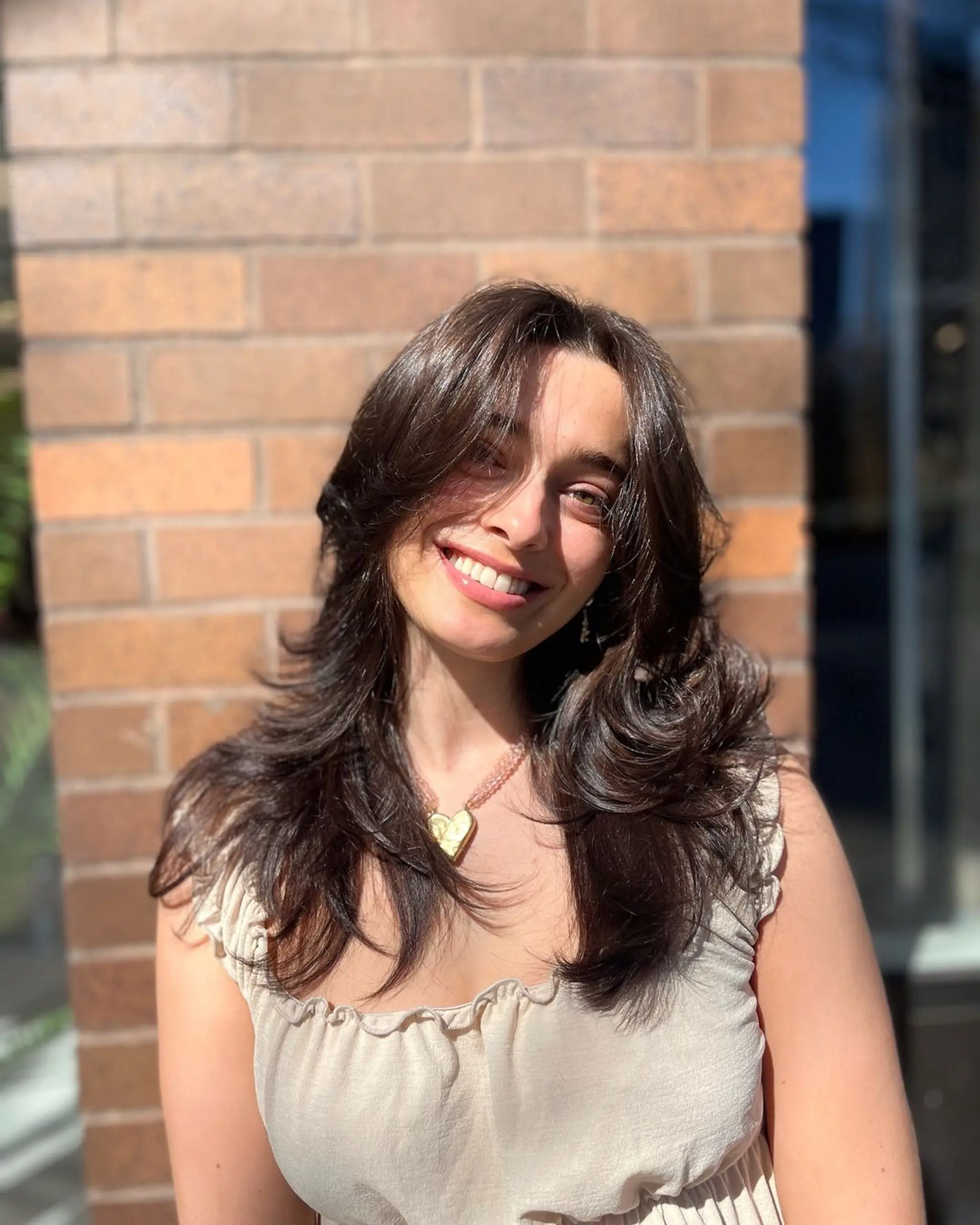 Long dark brown hair with straight texture, featuring voluminous layers, natural waves, and a shiny finish. Face-framing layers and a side part complete the look.
