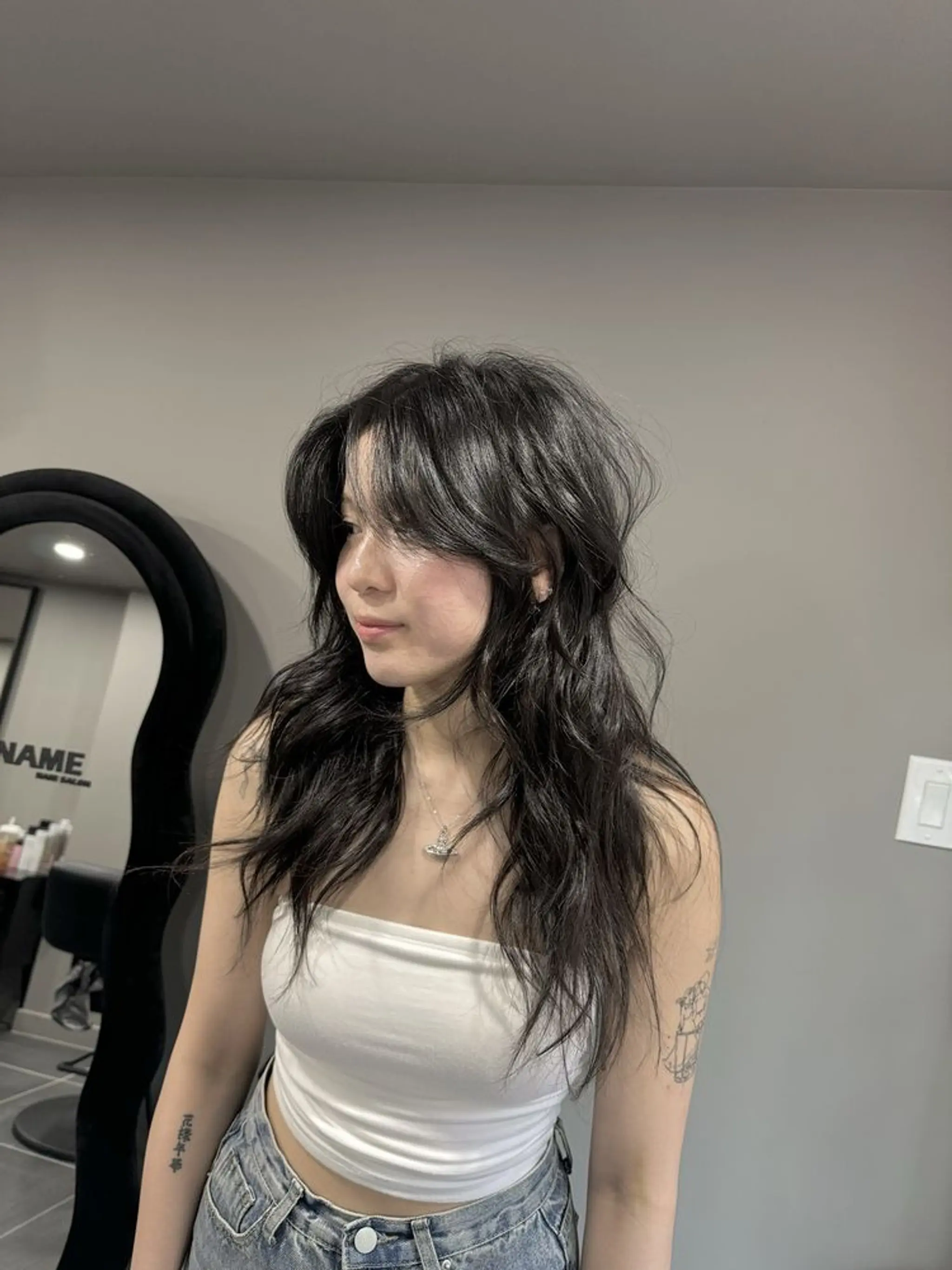 Long, wavy, dark brown hair with layers, tousled and voluminous, featuring face-framing wispy bangs.