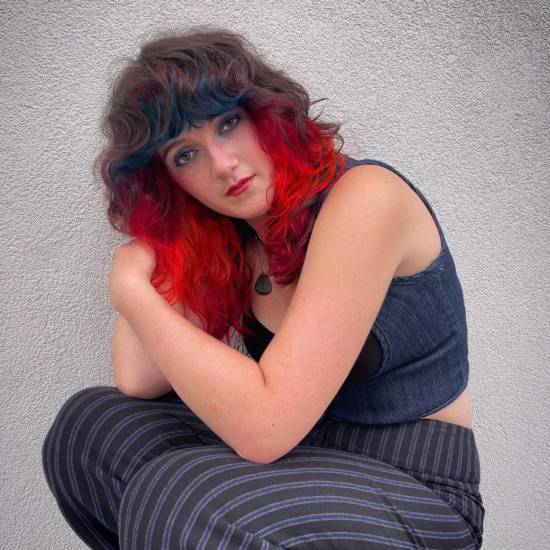 A textured mid-length shag haircut with wavy curtain-style bangs, featuring dark brown layered hair over vibrant red underlights and teal accents in the fringe. 1