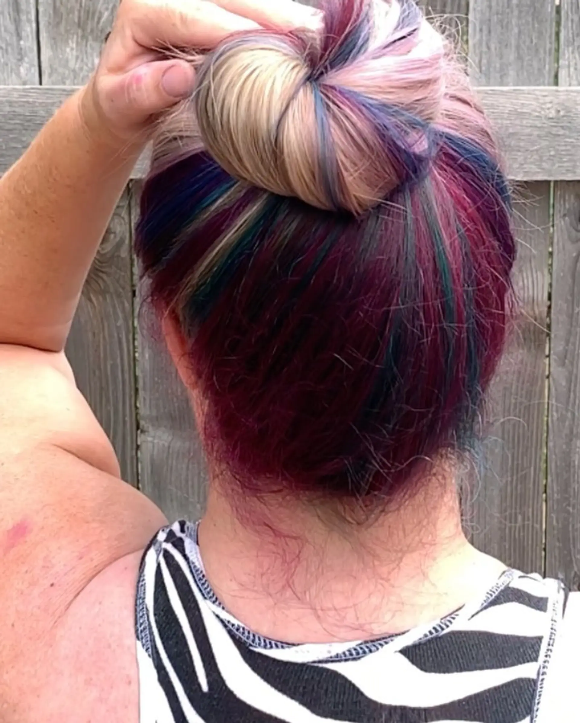 A high bun showcasing vivid multi-colored tones of magenta, purple, and teal underneath blonde highlights. 1