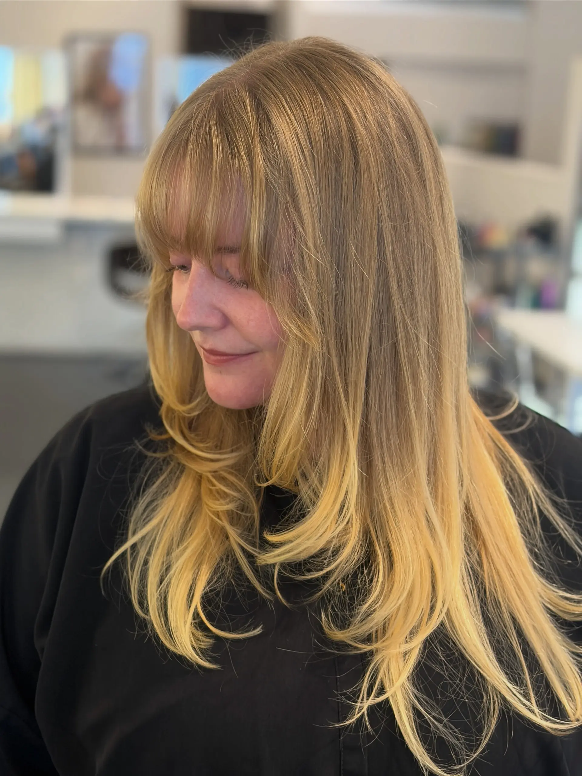 Long golden blonde hair styled with soft, face-framing layers and wispy straight-across bangs. 1