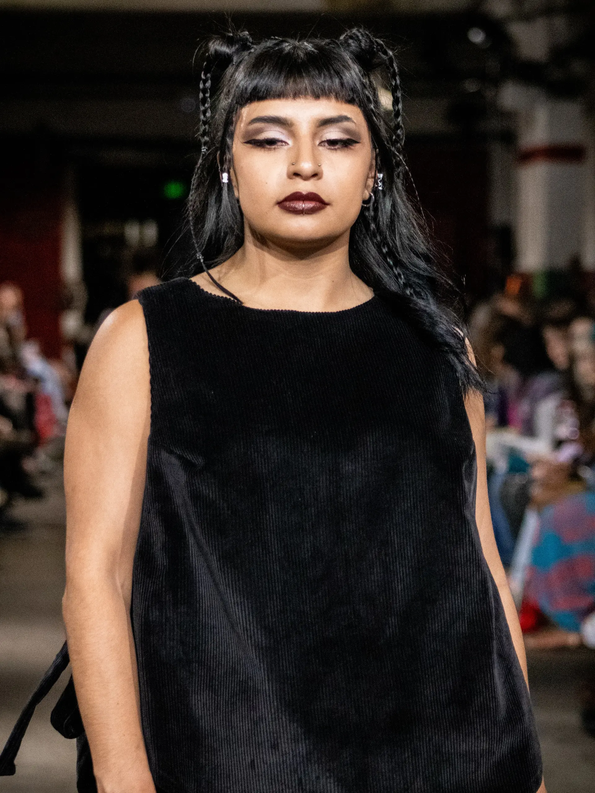 Fashion runway hairstyle showcasing blunt micro bangs, dual high braided buns, and fine face-framing braids on long dark waves. 1
